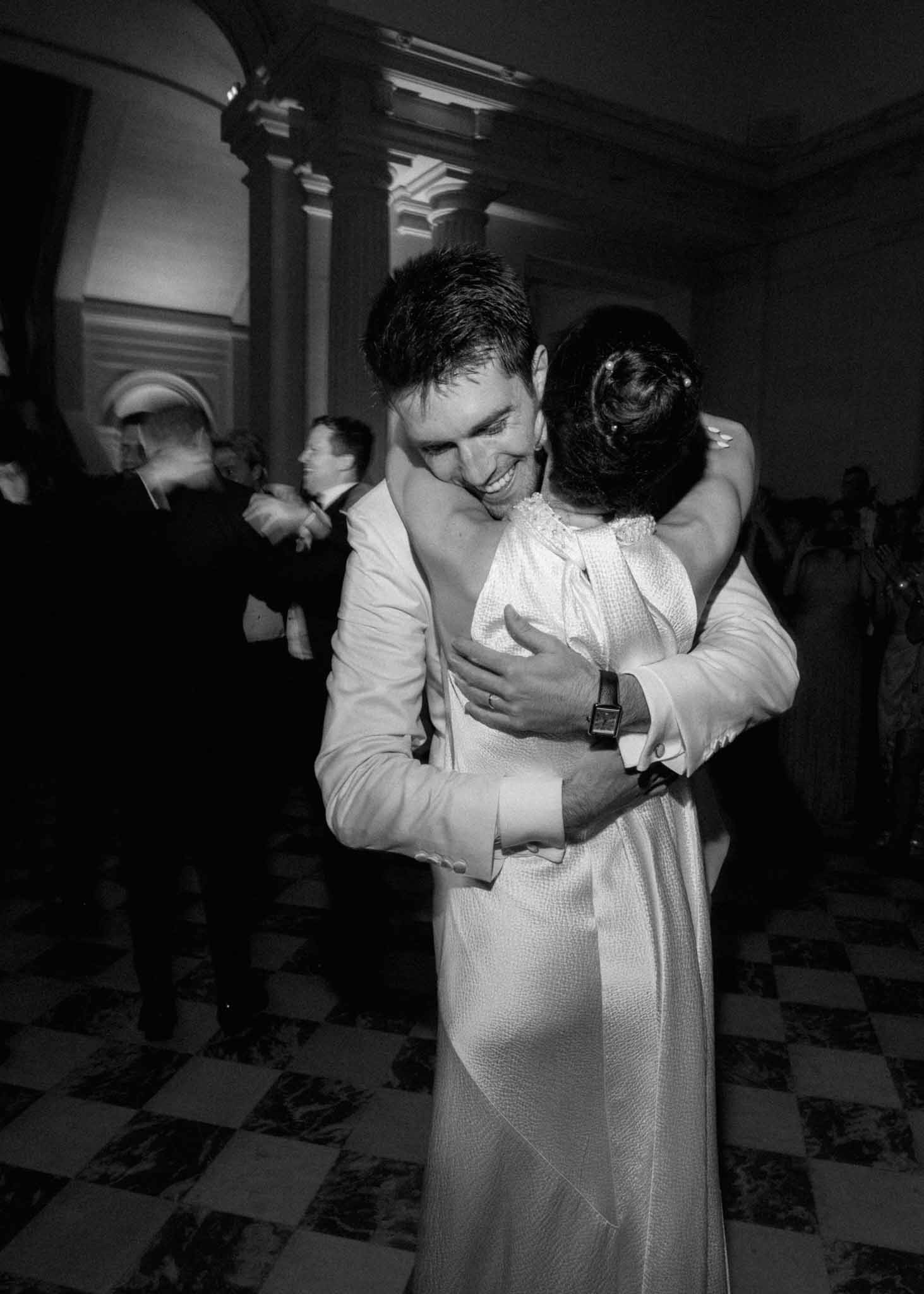 Black and white photo of couple dancing at reception in a ballroom with fluted columns and checkered floor
