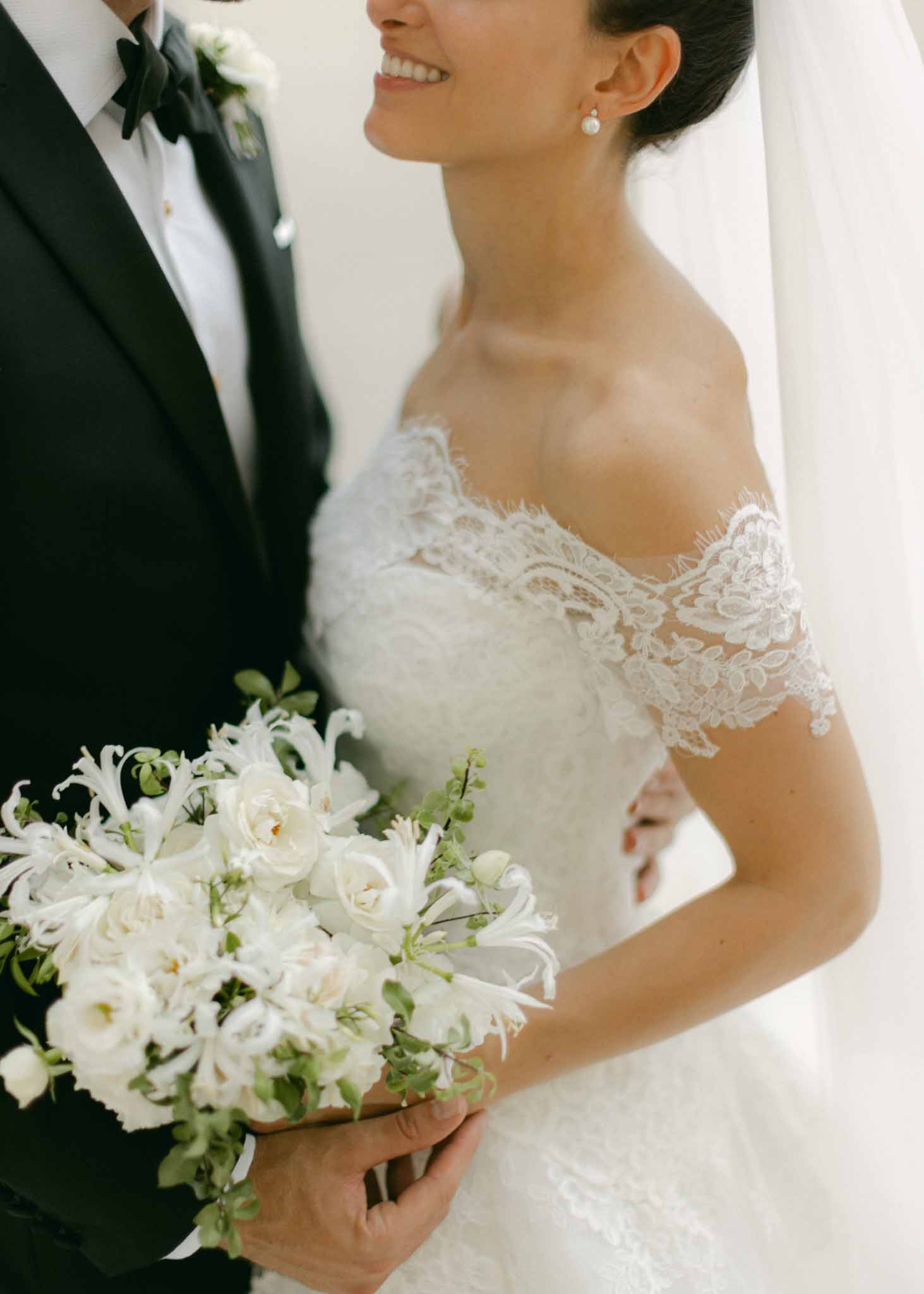 Bride in off-shoulder lace dress holding white bouquet at Chateau Saint-Martin photographed by H Clark
