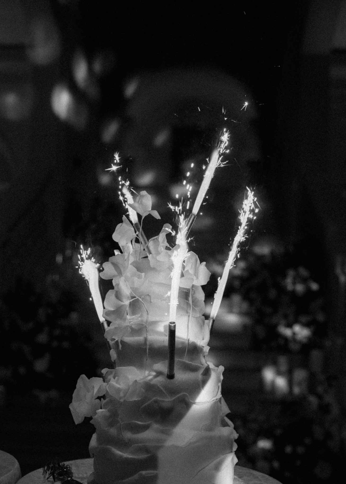 Multi-tiered wedding cake with ruffled fondant and orchid topper, sparkler candles lit against dark background