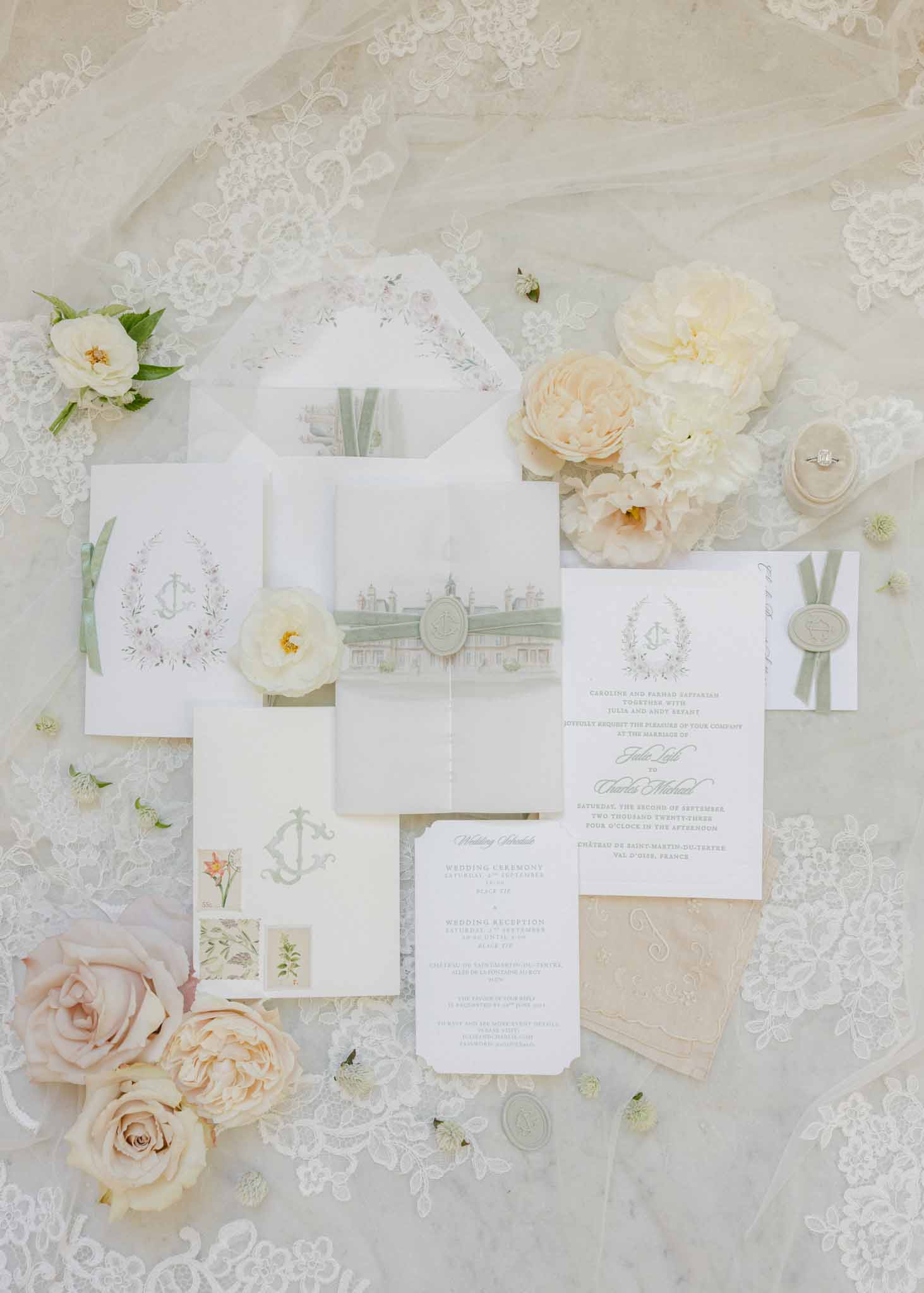 Flat lay of cream stationery with sage ribbon, wax seals, and blush garden roses on lace