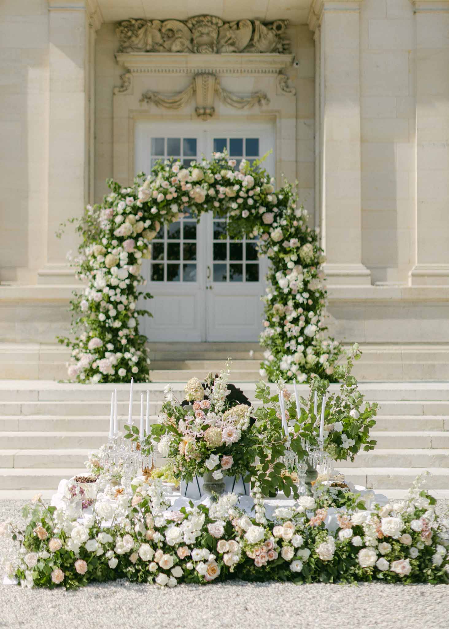 Floral arch of ivory roses and blush peonies framing neoclassical building entrance for ceremony