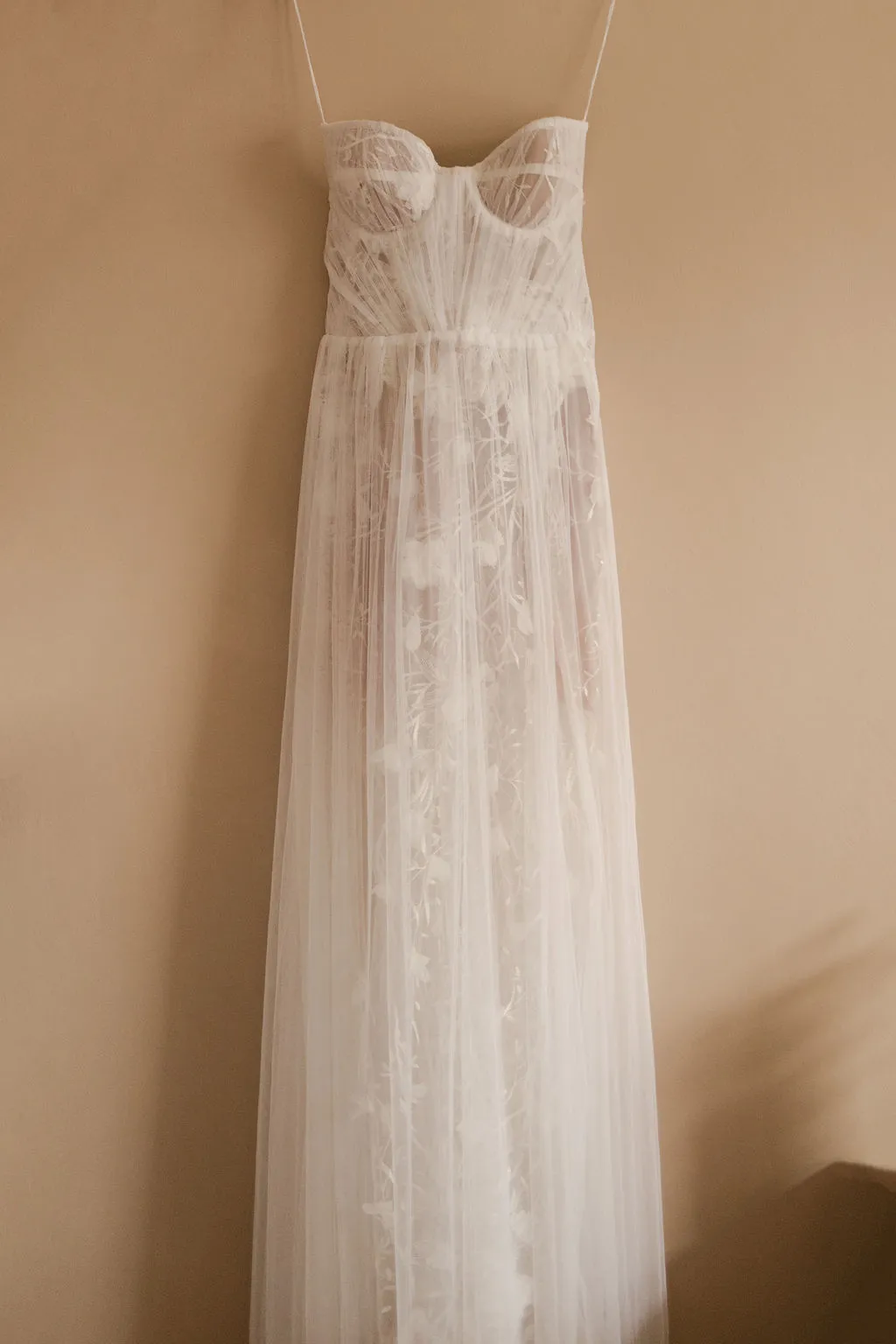 Ivory tulle A-line wedding dress with embroidered leaf motifs hanging on wall