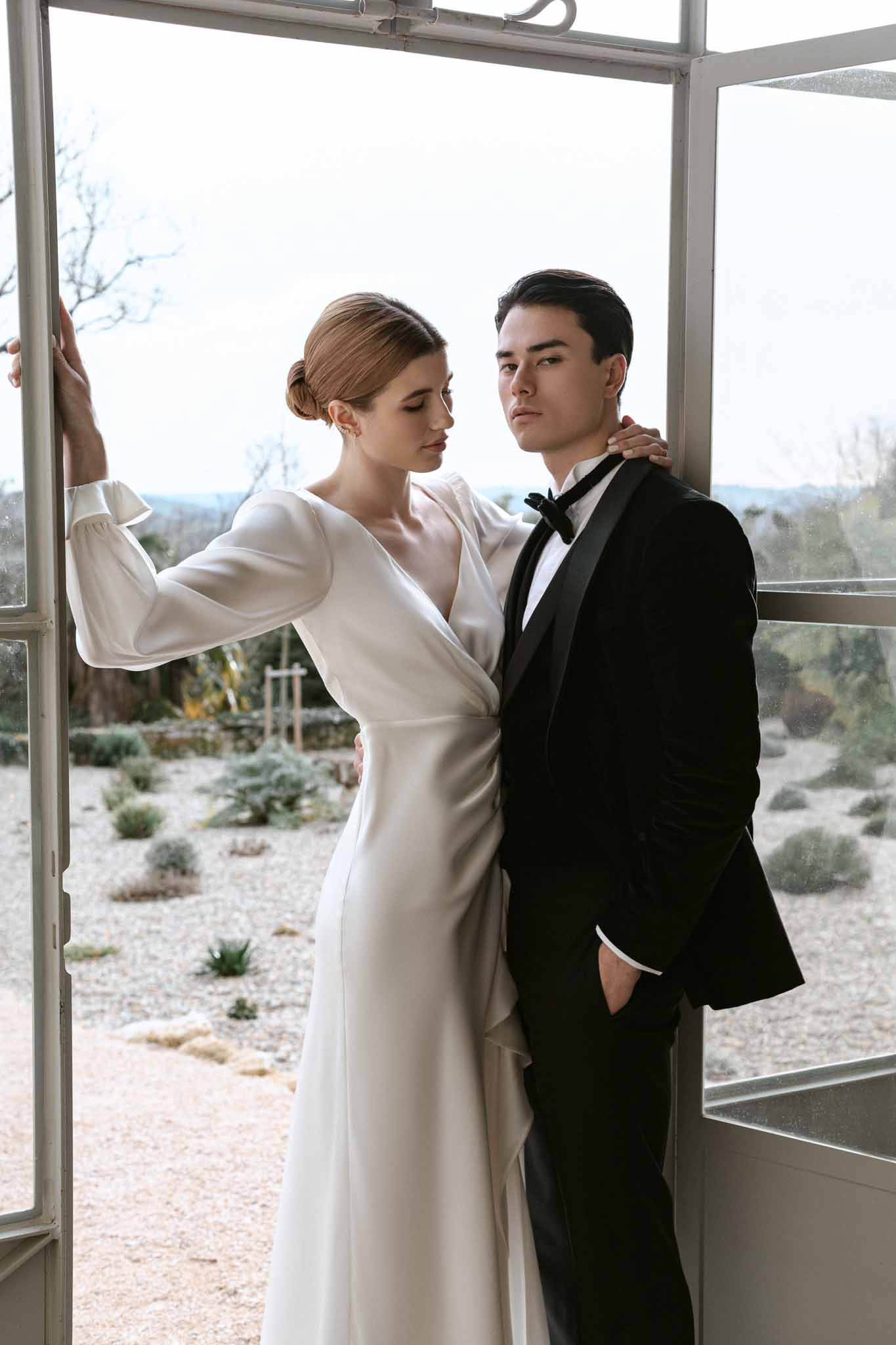 Bride and groom posing inside glass-walled structure during winter wedding