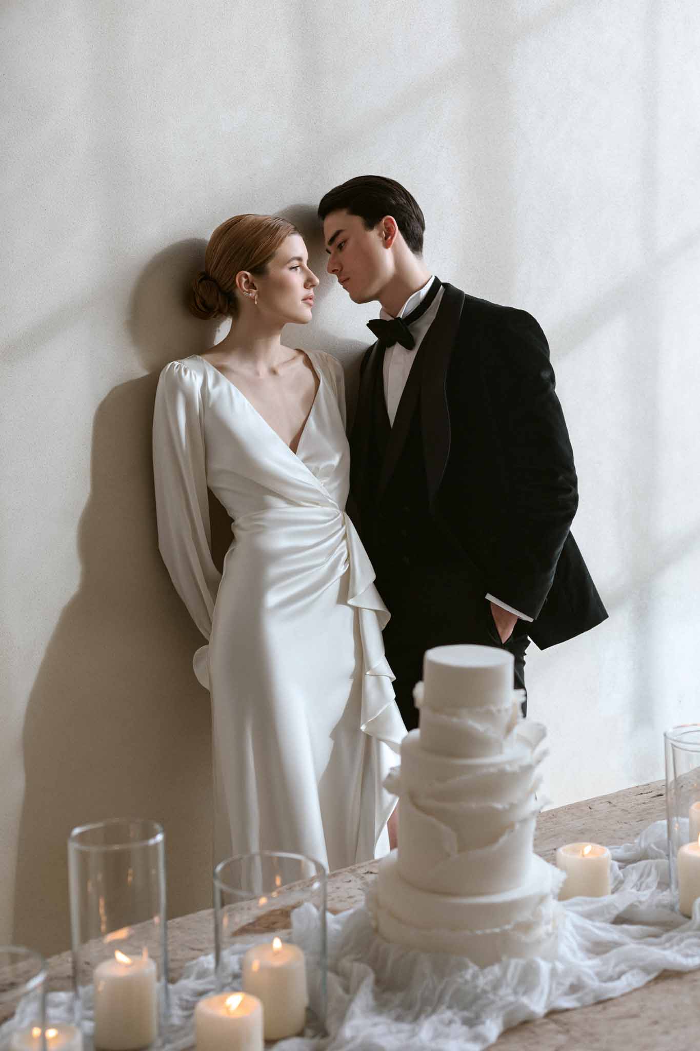 Bride and groom facing each other behind a multi-tiered white wedding cake with candles at a winter wedding