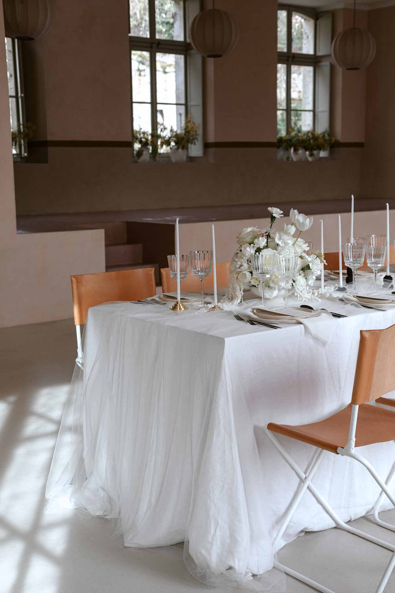 Long reception table with cognac leather chairs, brass candleholders, white roses, and paper lanterns overhead