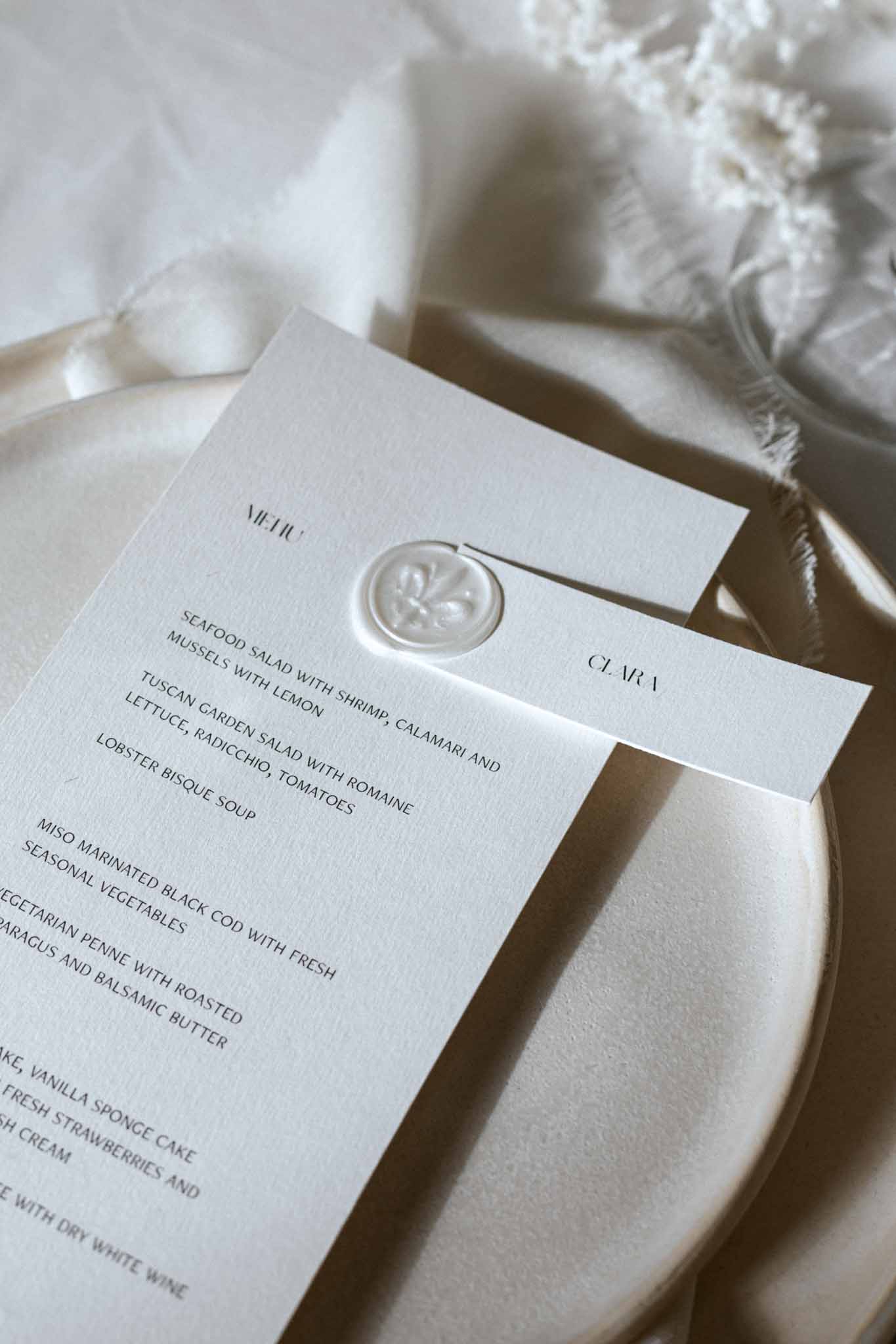 Close-up of reception menu card with wax seal on white fringed napkin and plate
