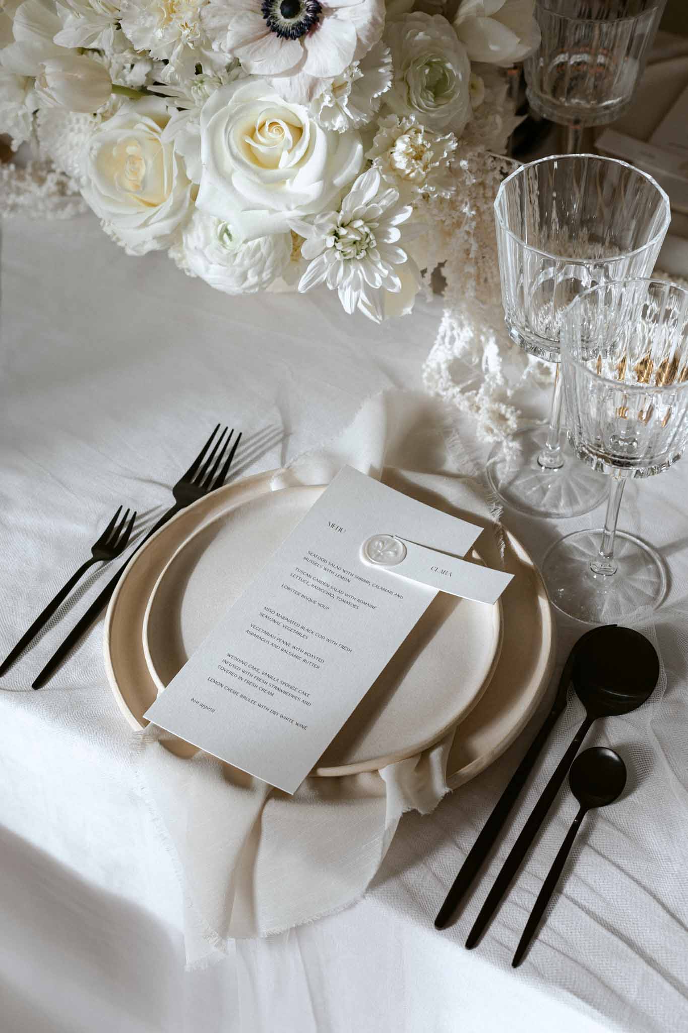 Winter reception place setting with black flatware, white roses, anemones, and crystal glassware