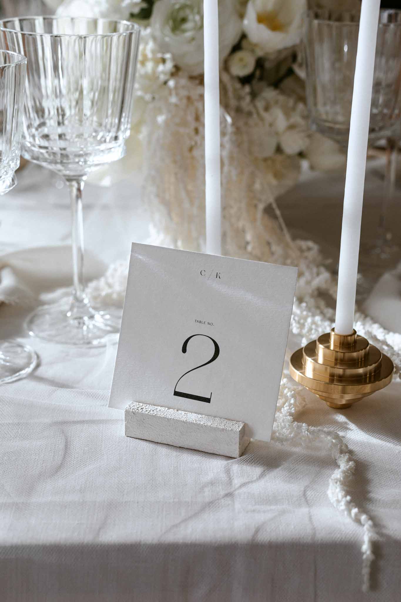 Reception table place setting with lace runner, crystal glasses, brass candlesticks, and table number card