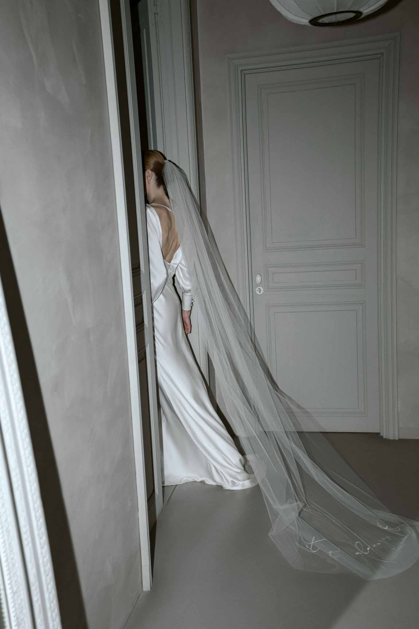 Bride from behind in ivory open-back gown with embellished tulle veil in modern interior