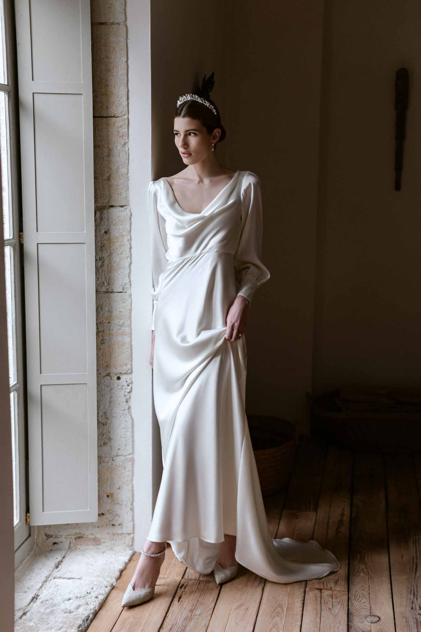 Bride in ivory silk cowl dress with beaded tiara posing in historic stone building