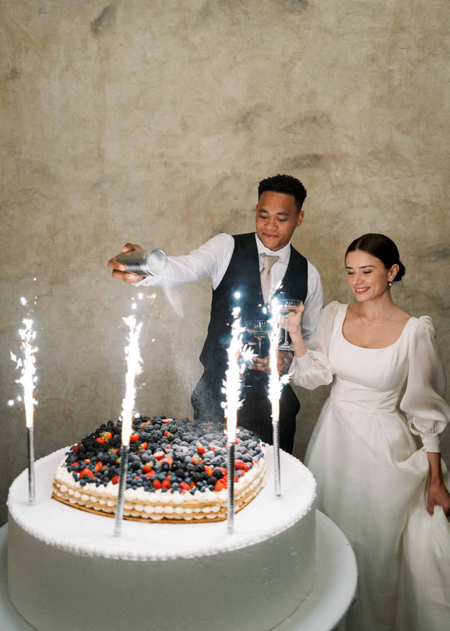 Bride and groom beside heart-shaped berry tart cake with lit sparklers at indoor reception