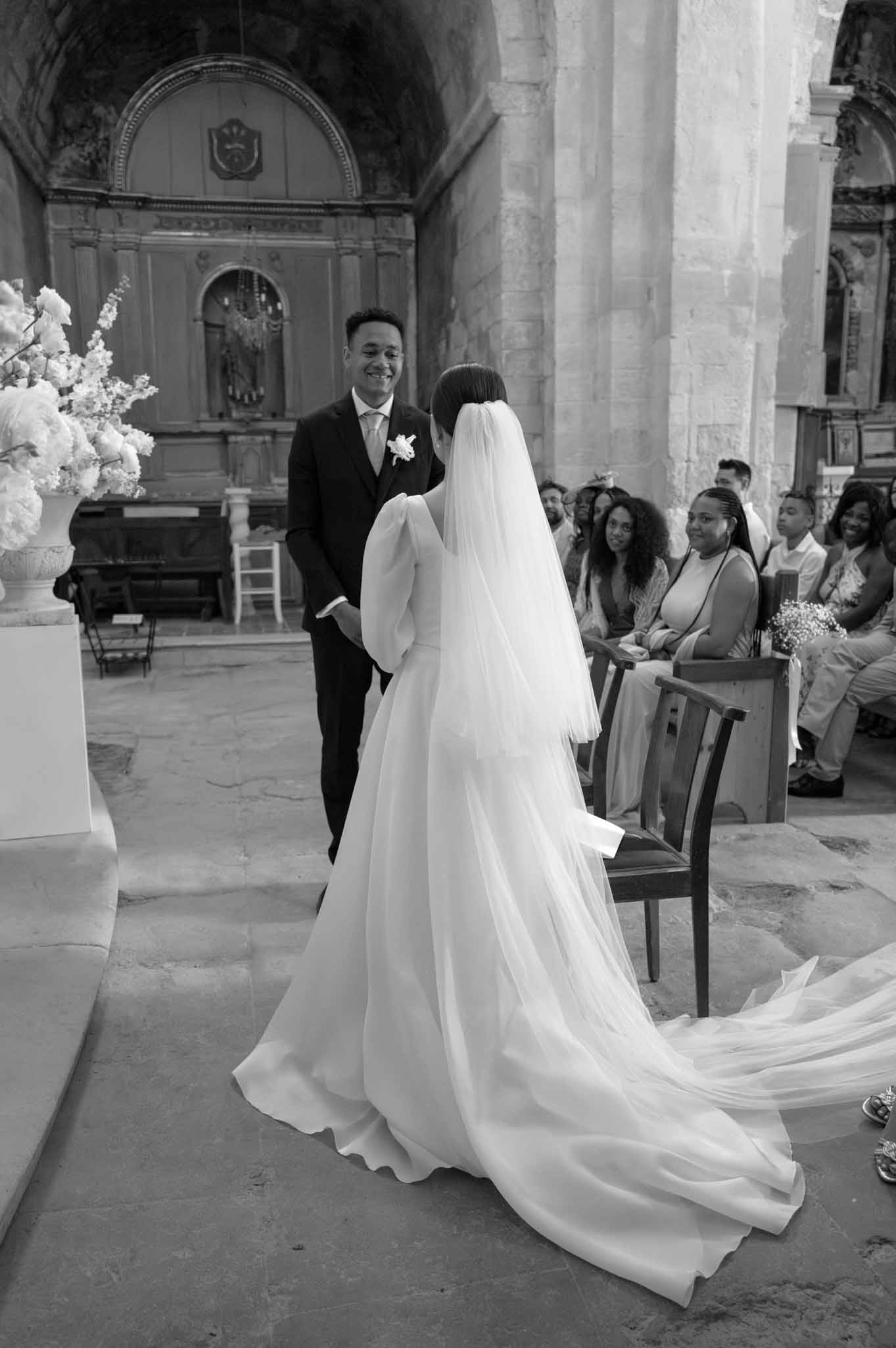 Black and white ceremony in stone chapel with bride's cathedral veil trailing across floor