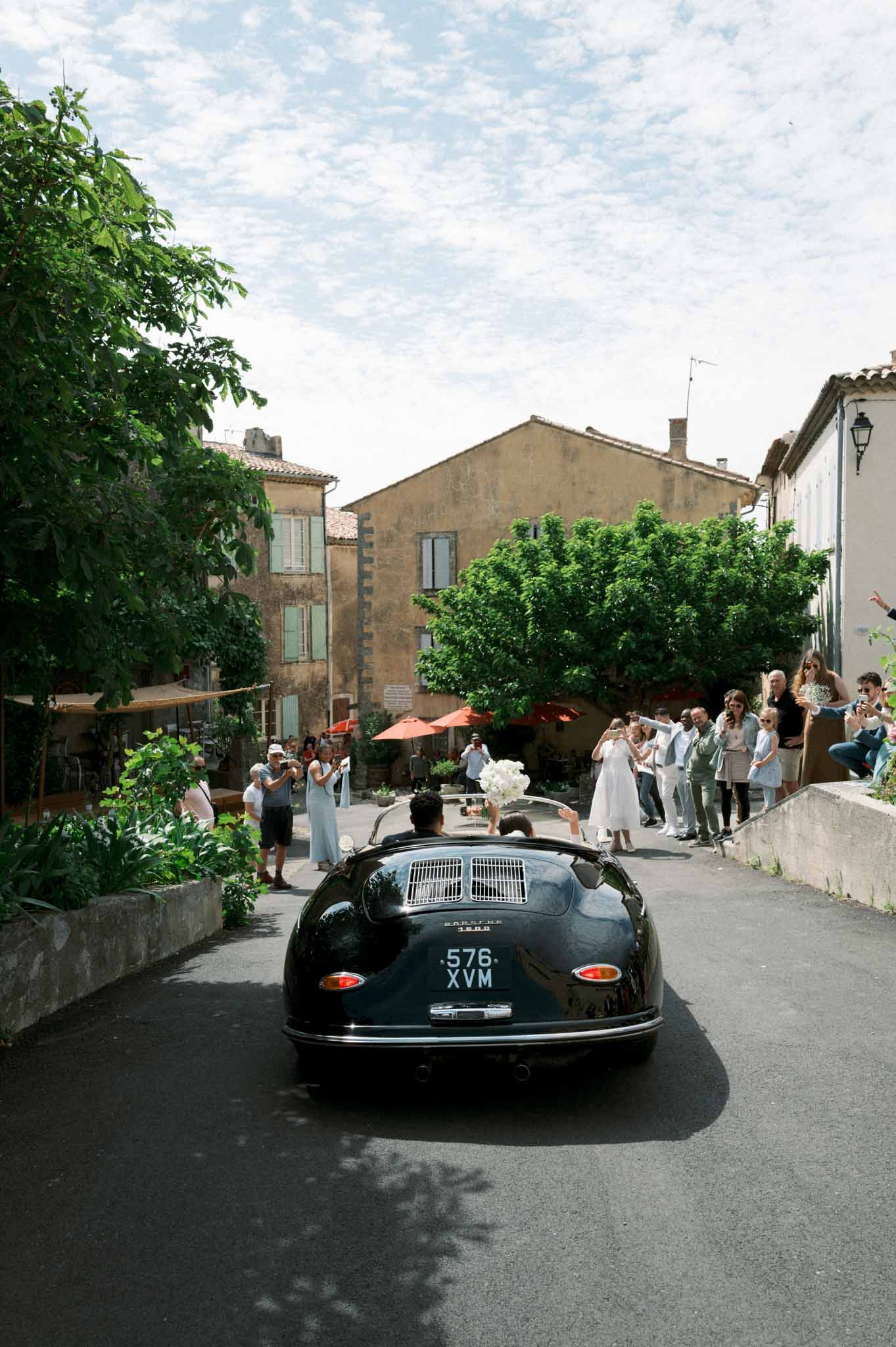 Bride and groom departing in vintage green Porsche convertible through Provencal village street lined with guests