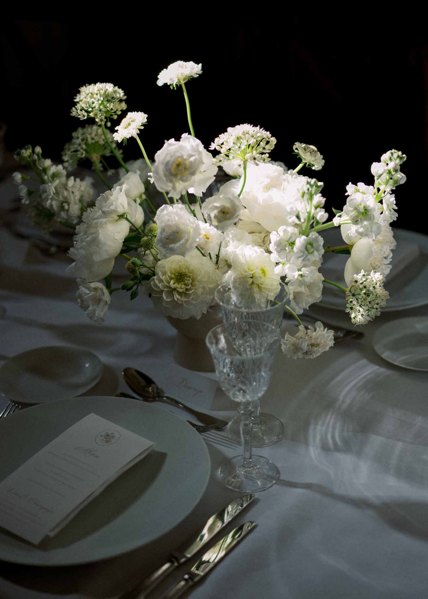 All-white floral centerpiece of peonies and dahlias with monogram menu card and crystal goblets