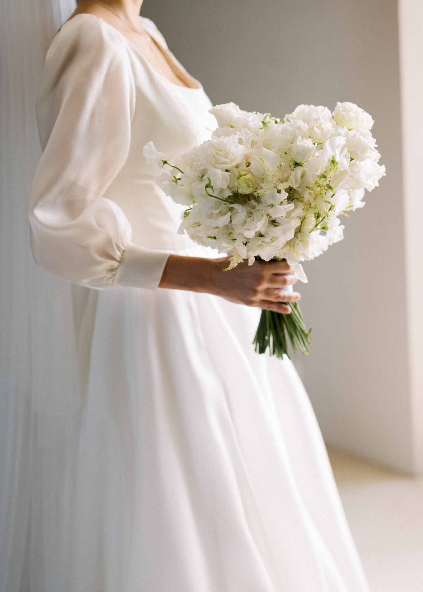 Bride in puff-sleeve satin gown holding all-white sweet pea and lisianthus bouquet