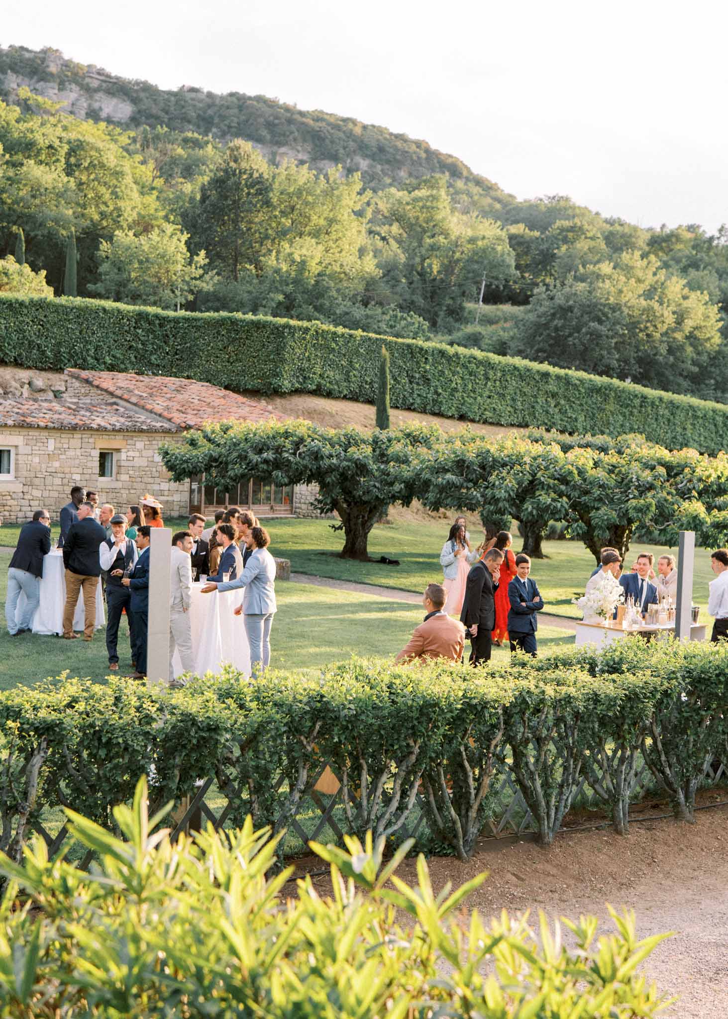 Guests mingling on manicured lawn during cocktail hour at a Provencal stone estate in golden hour light