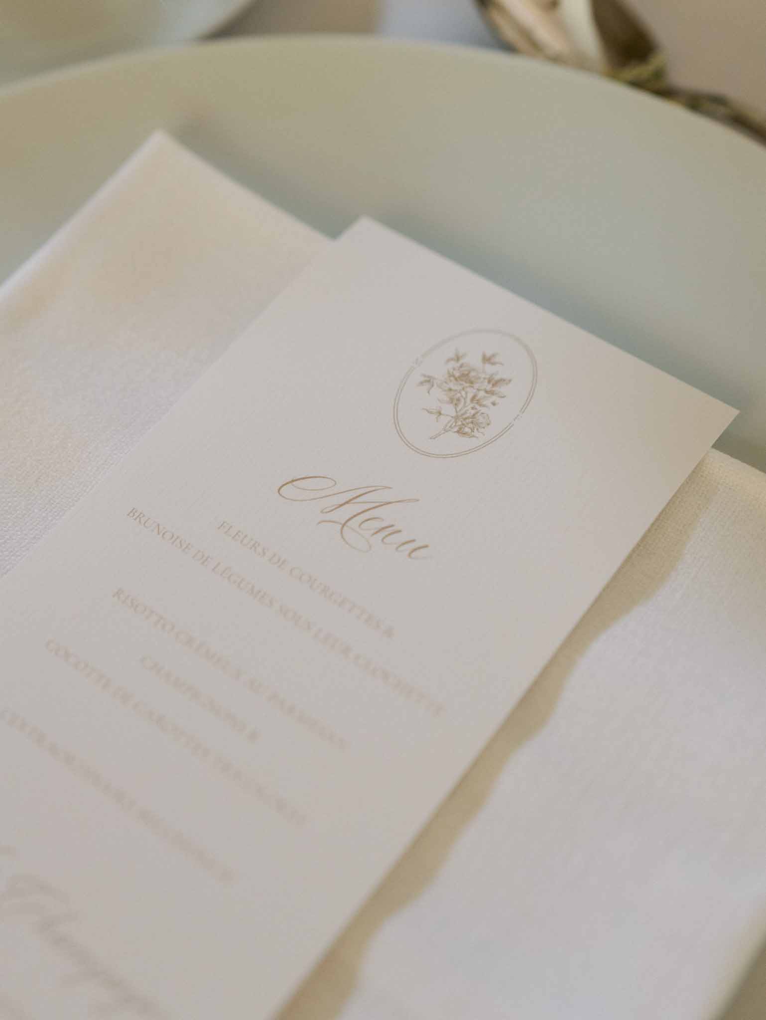 Wedding reception menu card in gold typography on cream paper placed on sage green charger plate