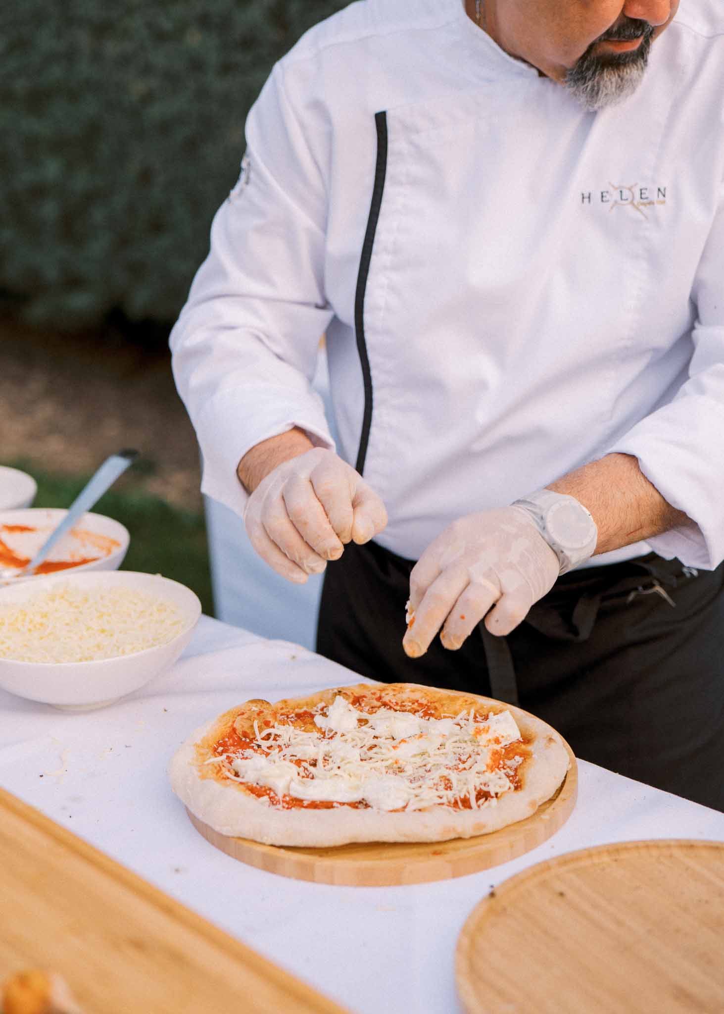Chef in white jacket prepares a pizza on a wooden board at an outdoor wedding food station
