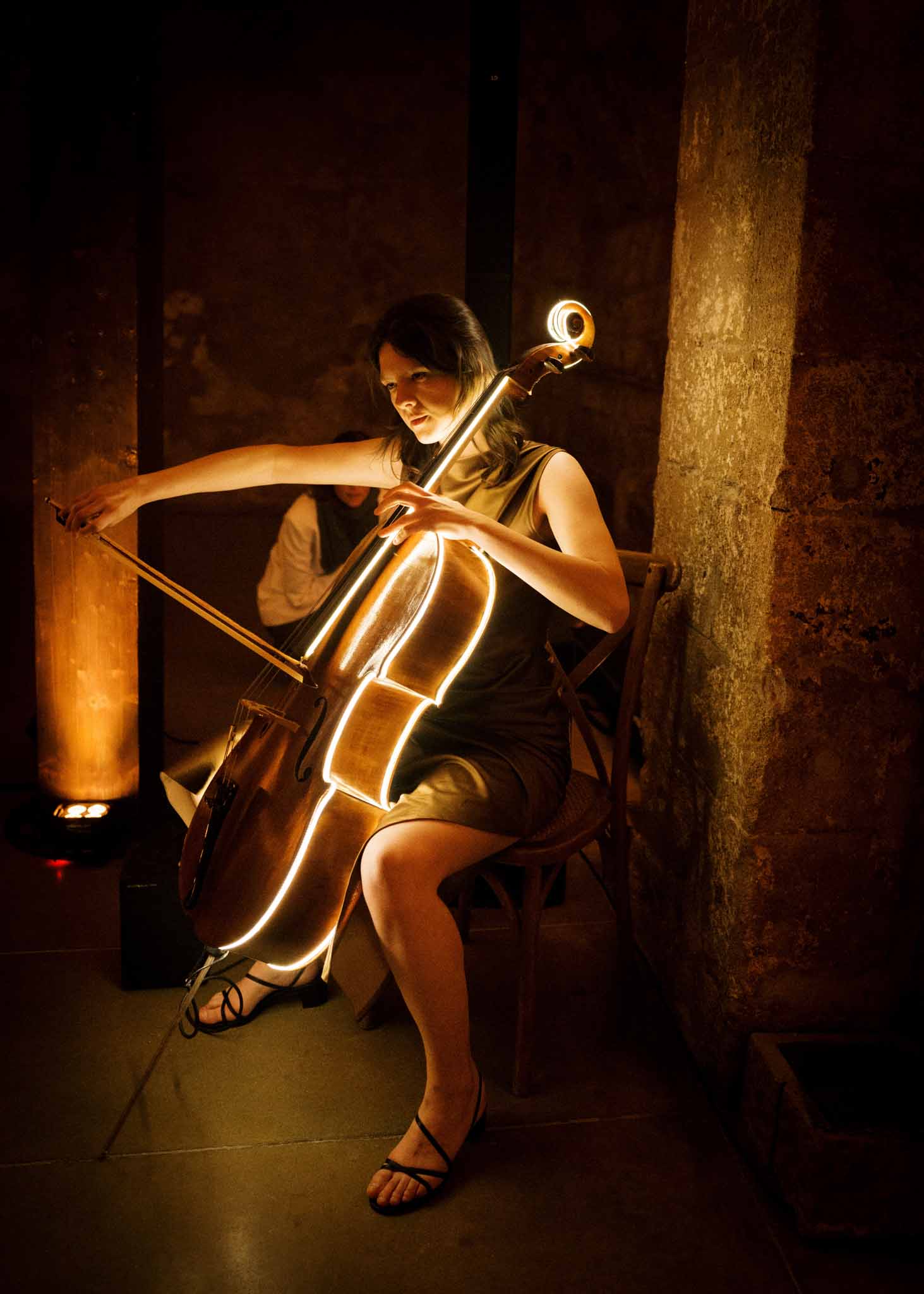 Cellist performing with LED-lit cello in a dimly lit stone chateau interior during wedding reception