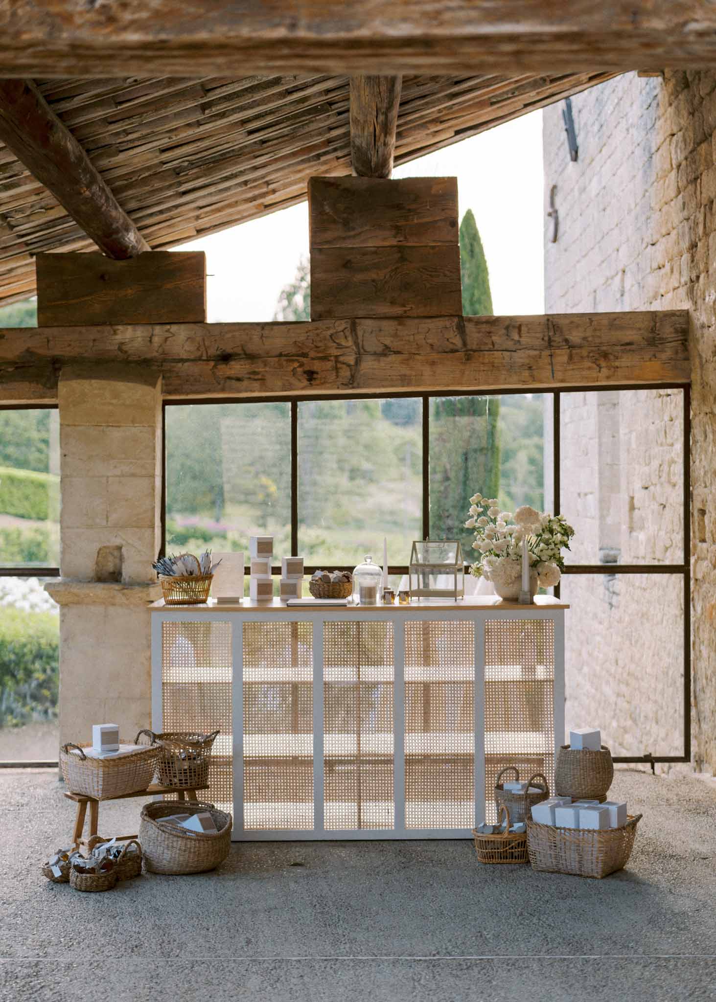 Welcome favor station with rattan baskets and white rose arrangement in stone-beamed structure