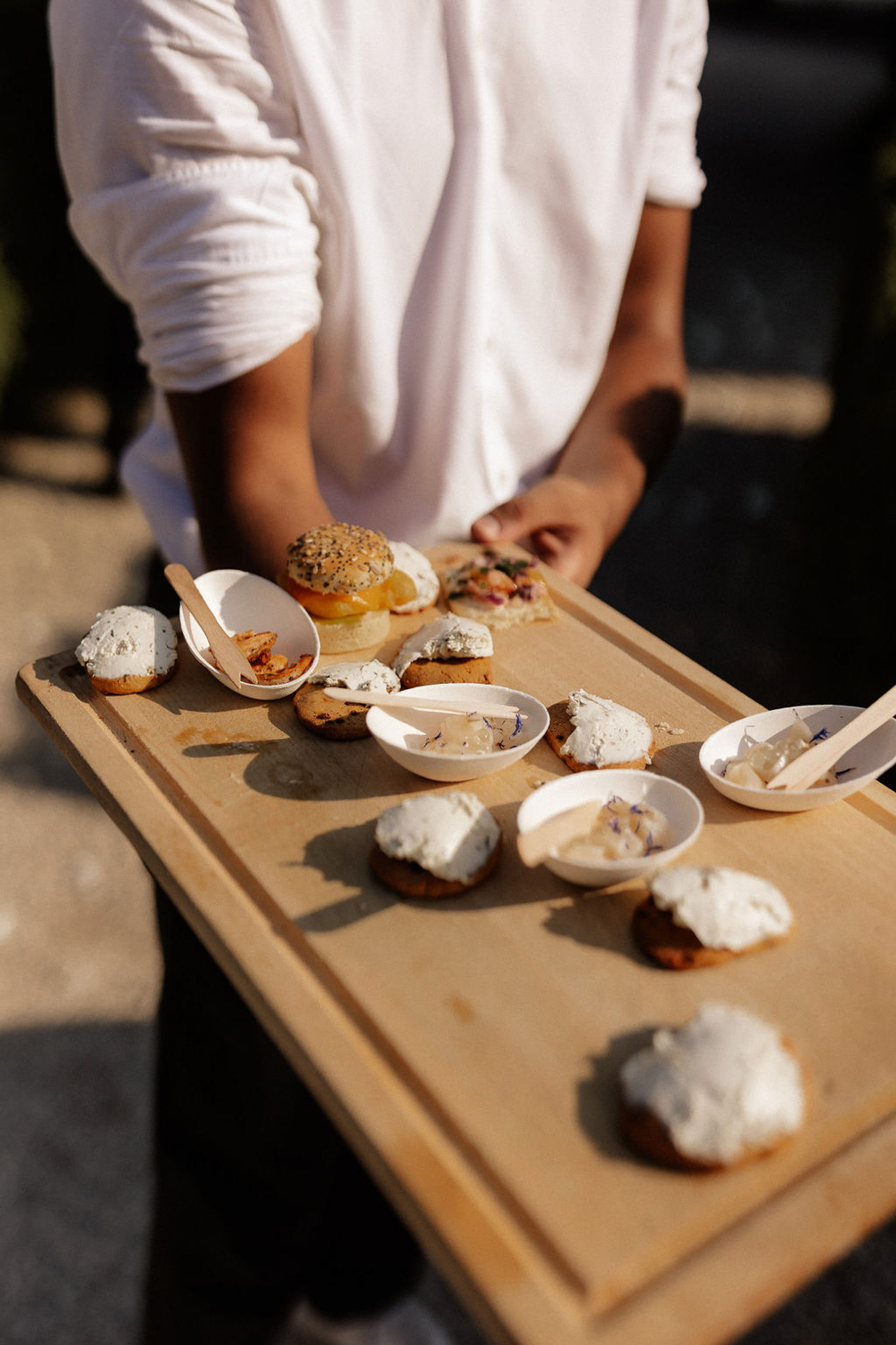 Server presenting canapés and appetizers on wooden board during cocktail hour at wedding reception