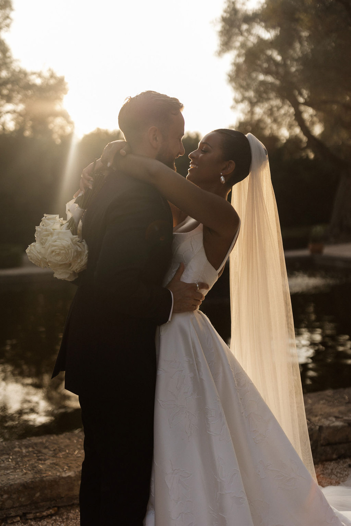 Bride and groom embracing during golden hour portrait session on tree-lined path