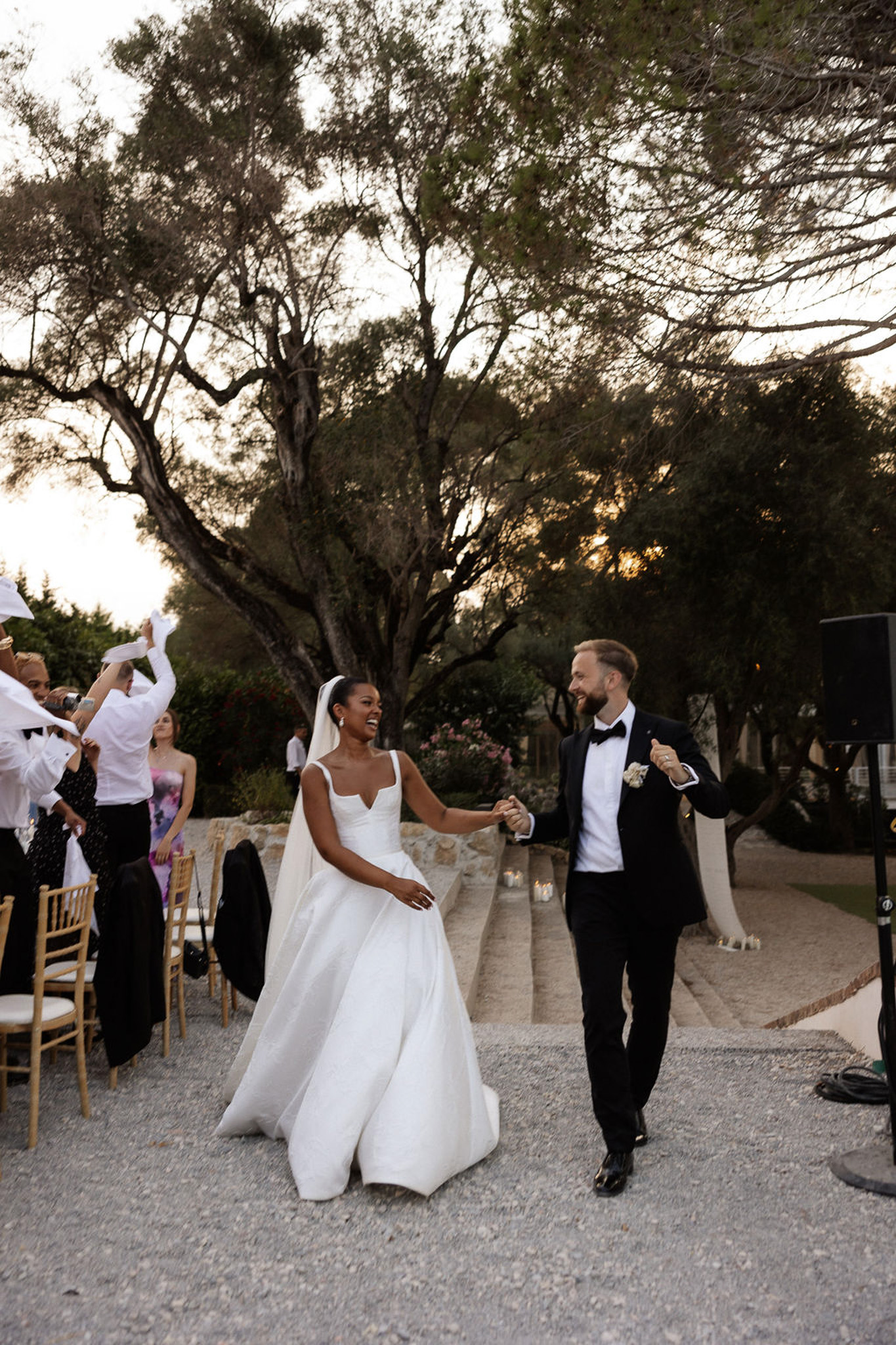 Bride and groom walking down pathway with guests celebrating at outdoor garden reception venue