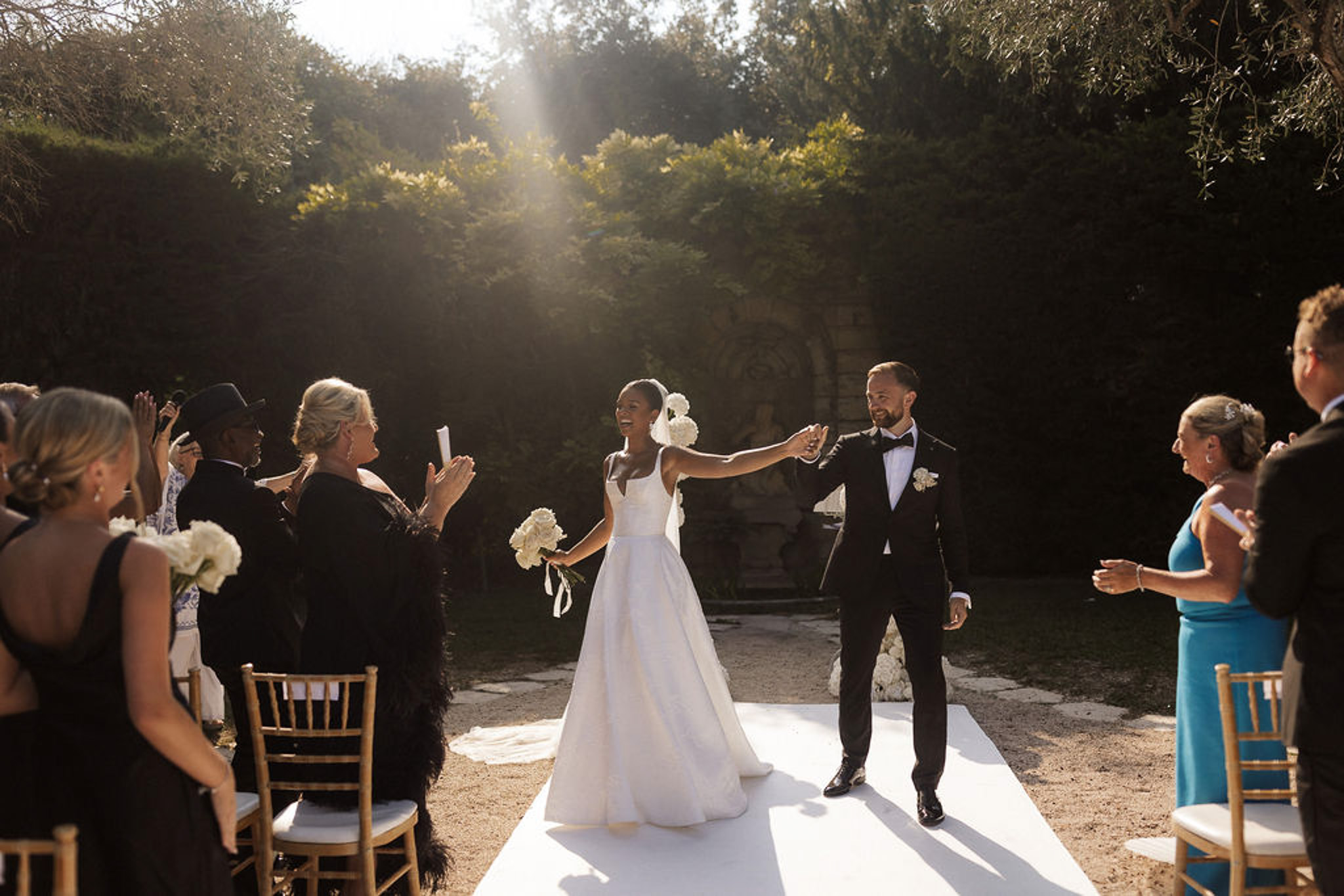 Bride and groom walking down aisle after outdoor garden ceremony with guests seated on wooden chairs