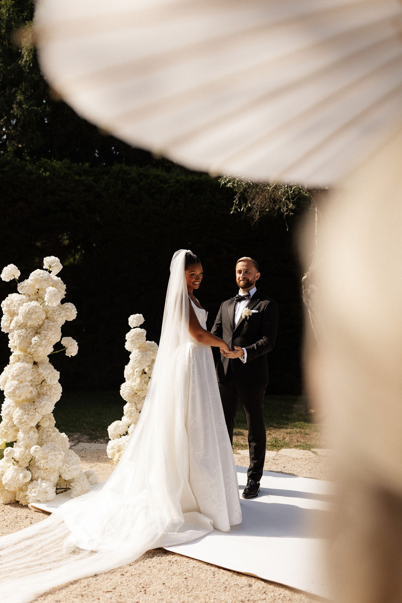 Bride and groom exchanging vows during outdoor garden wedding ceremony with white floral installations