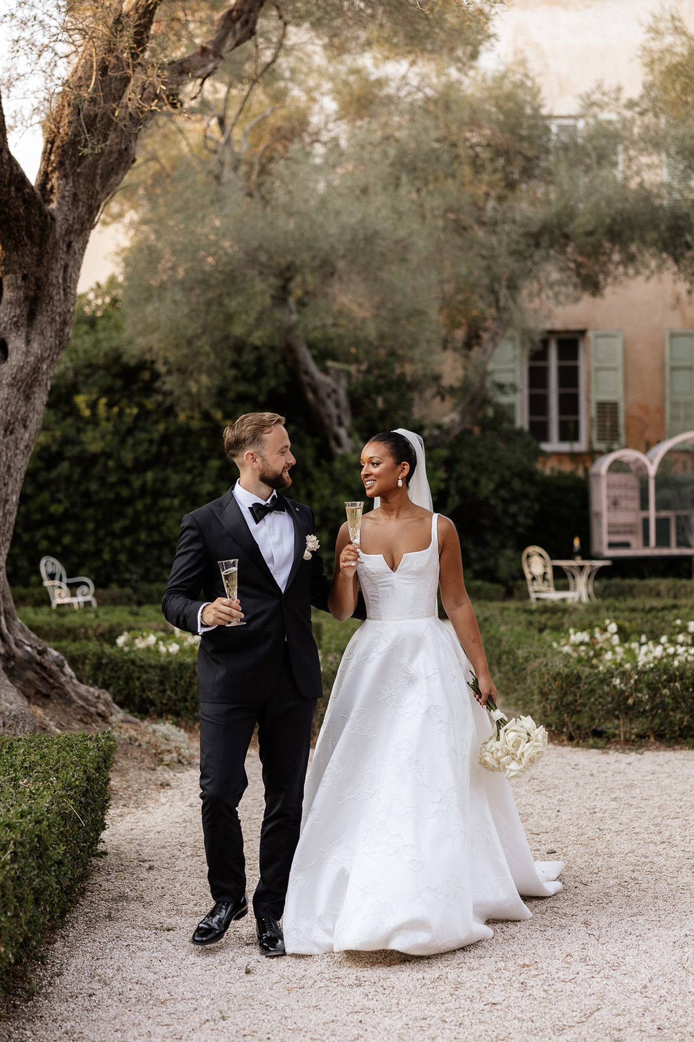 Couple walking with champagne flutes during reception in European garden courtyard