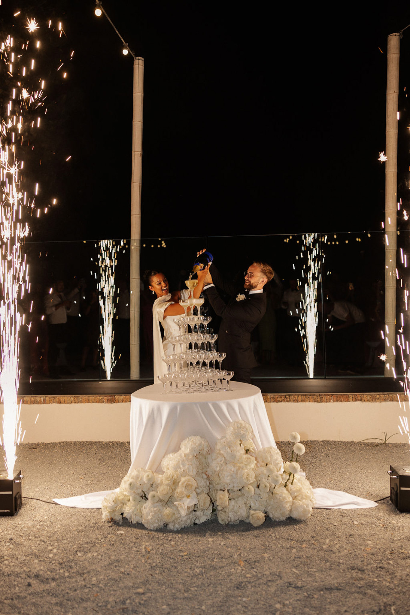 Bride and groom champagne tower ceremony with sparklers at outdoor evening reception