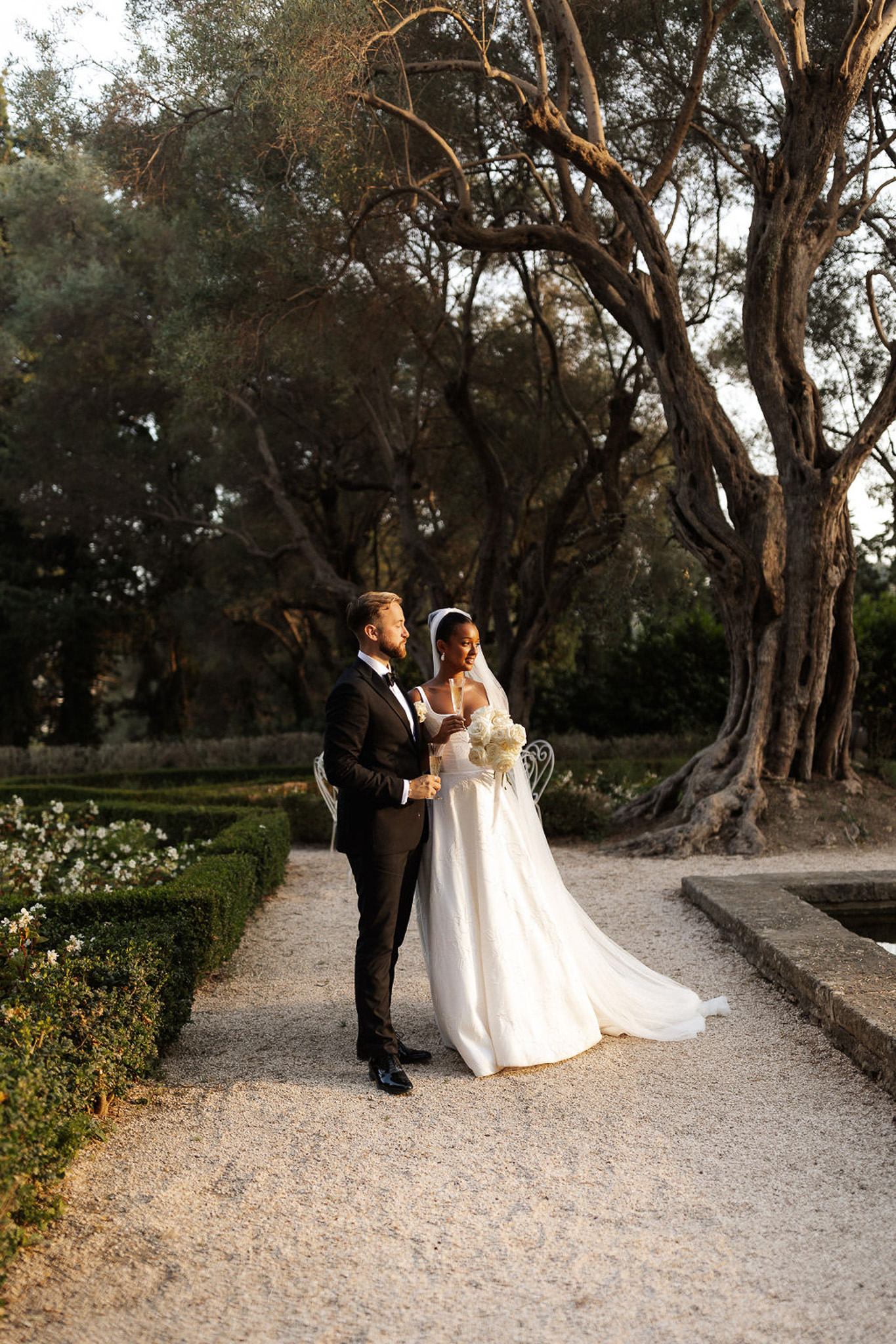 Bride and groom walking together along tree-lined pathway at garden estate