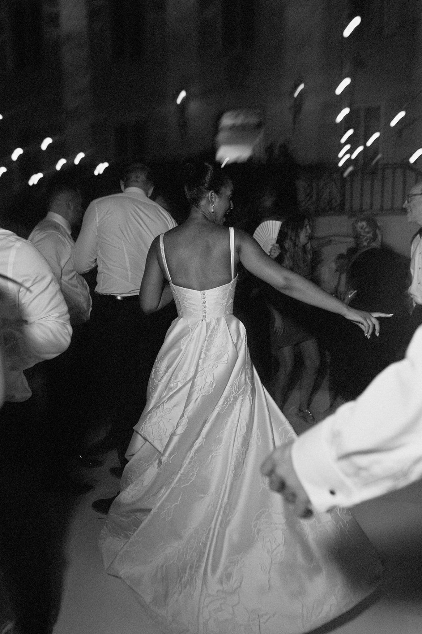 Bride dancing with guests at indoor wedding reception with string lighting