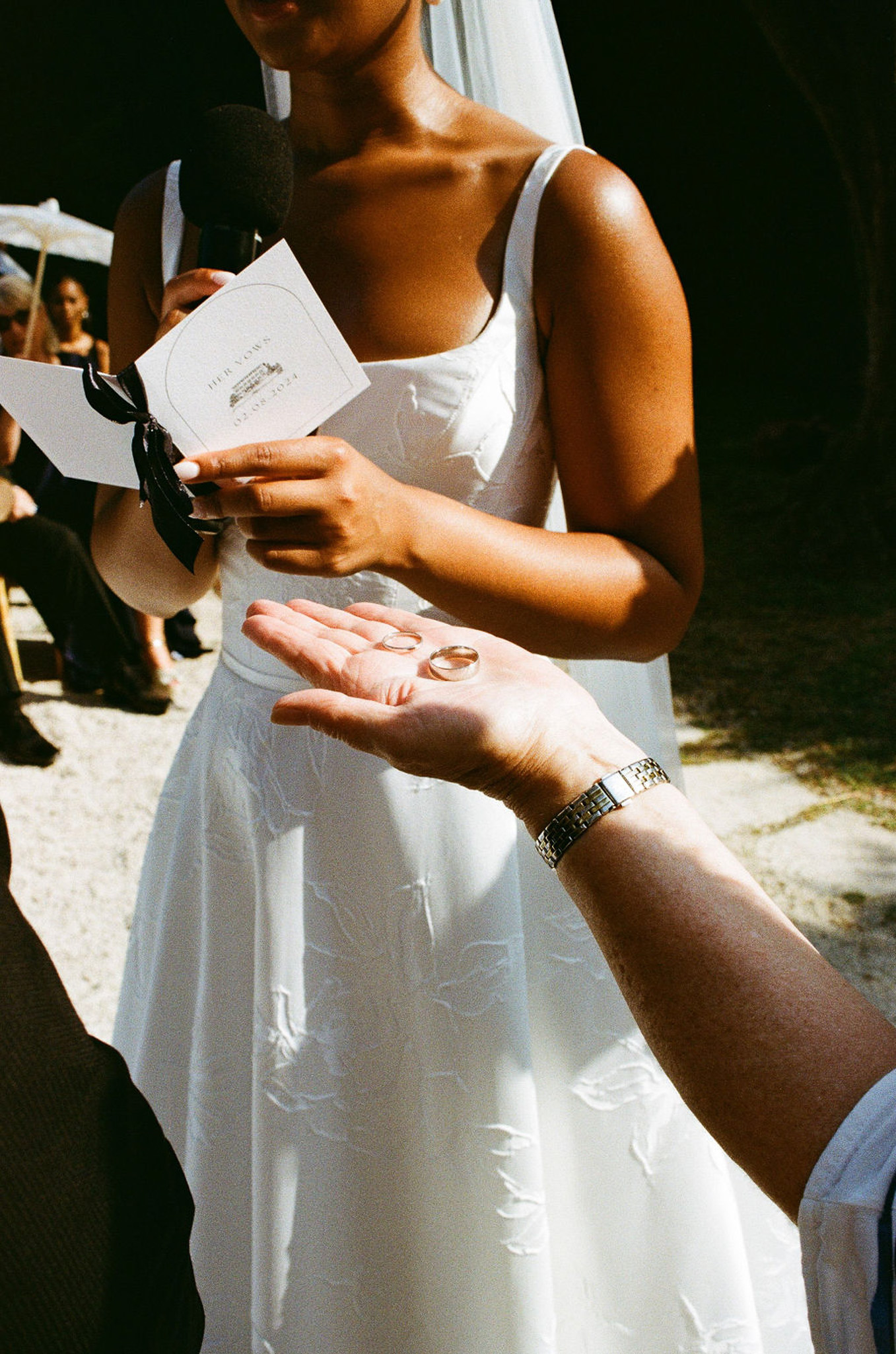Bride holding wedding rings and ceremony program during outdoor wedding ceremony