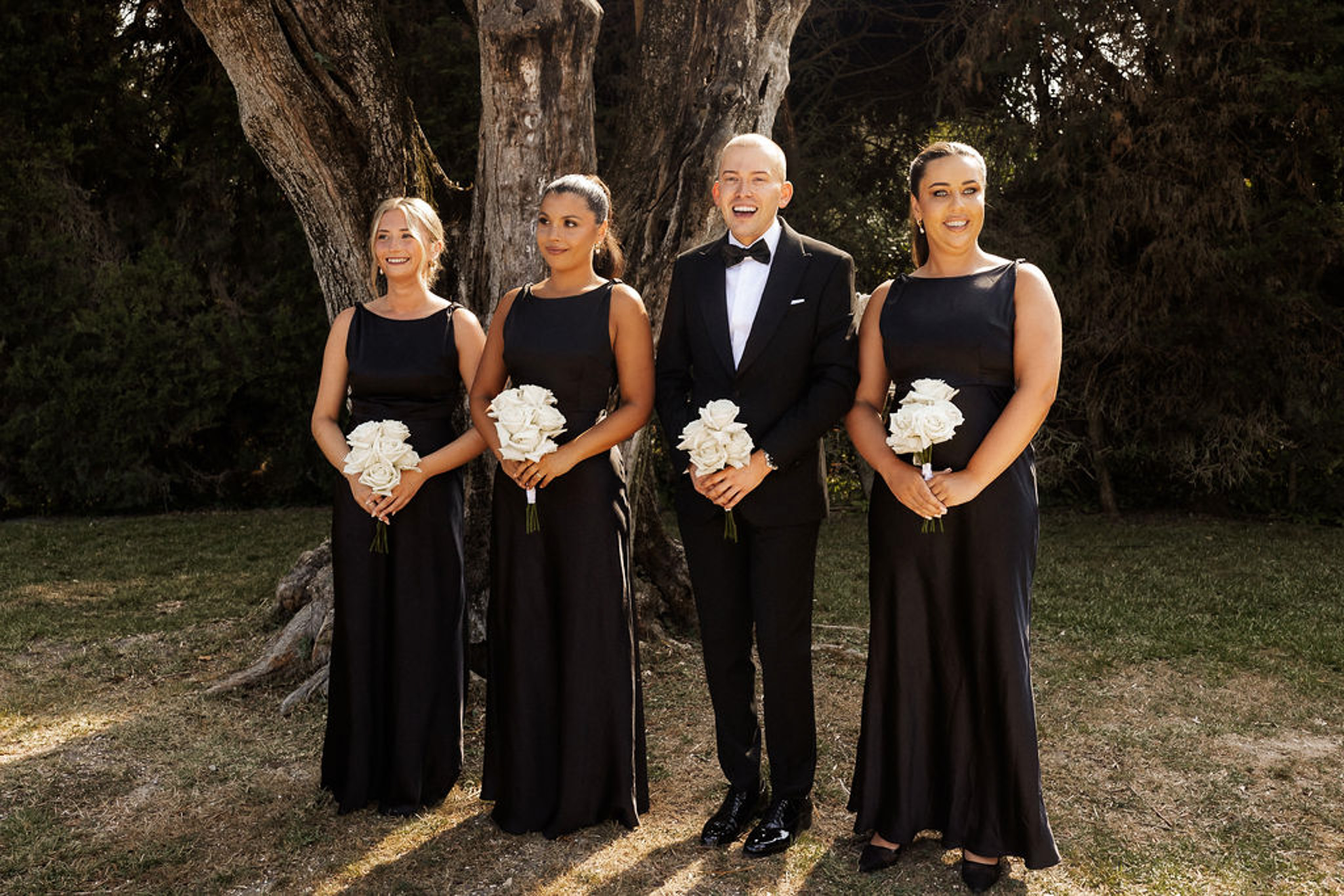 Bridal party portrait with groom and bridesmaids under tree in garden setting