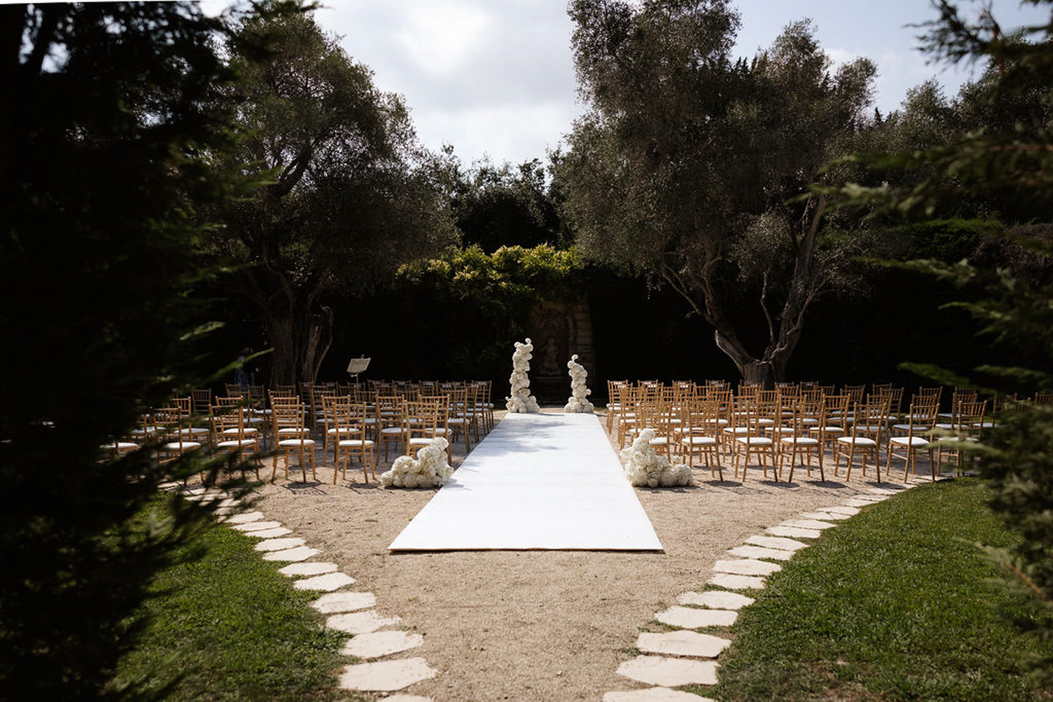 Wedding ceremony setup with white aisle runner and chairs in Mediterranean garden with olive trees