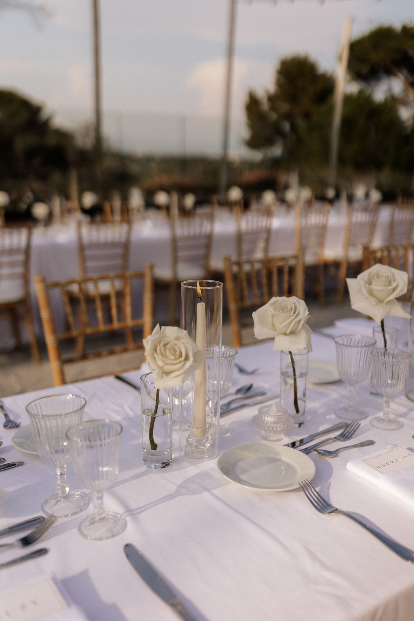 White reception table setting with roses and clear glassware at outdoor wedding venue
