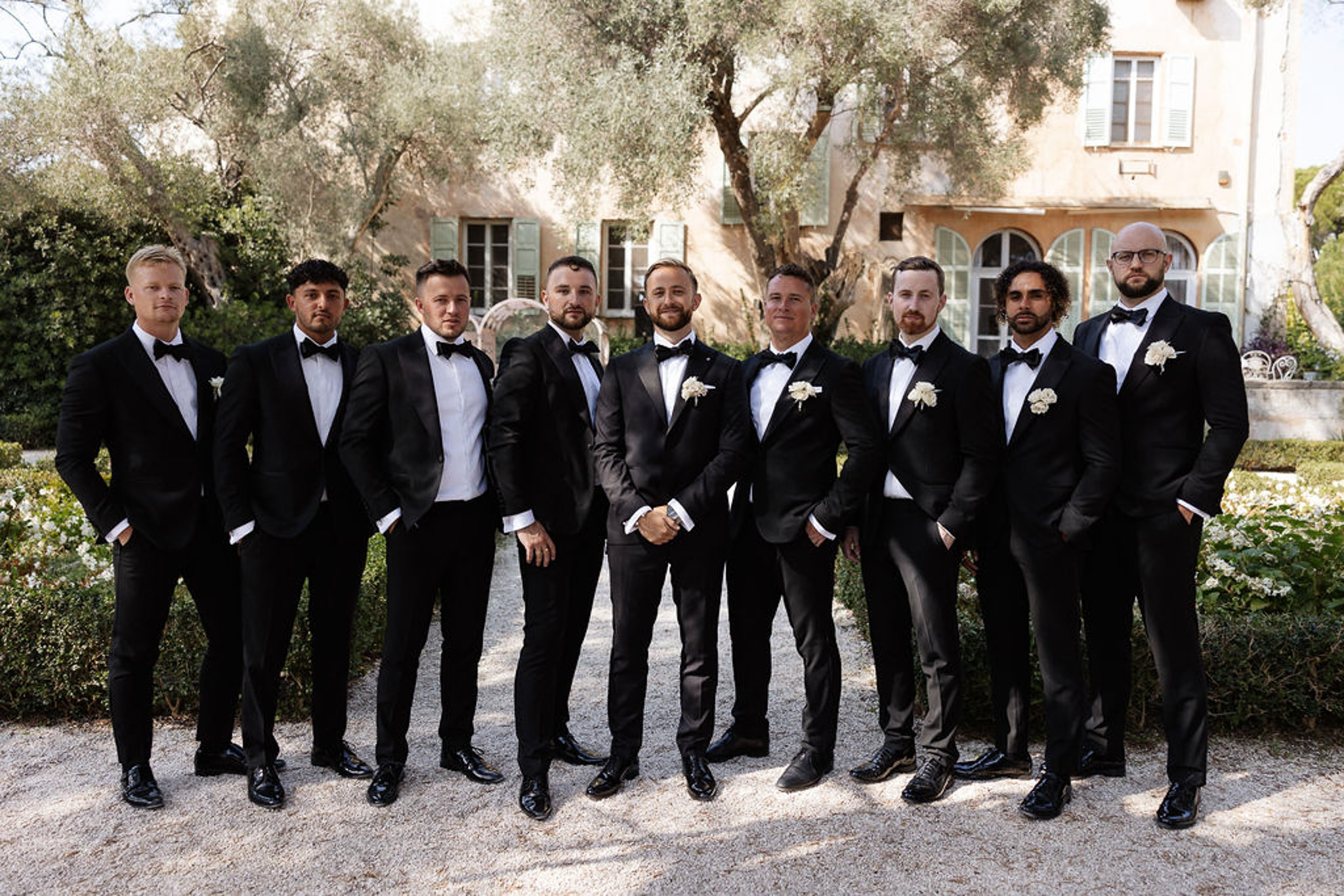 Groom and groomsmen in black tuxedos group portrait at Mediterranean villa courtyard