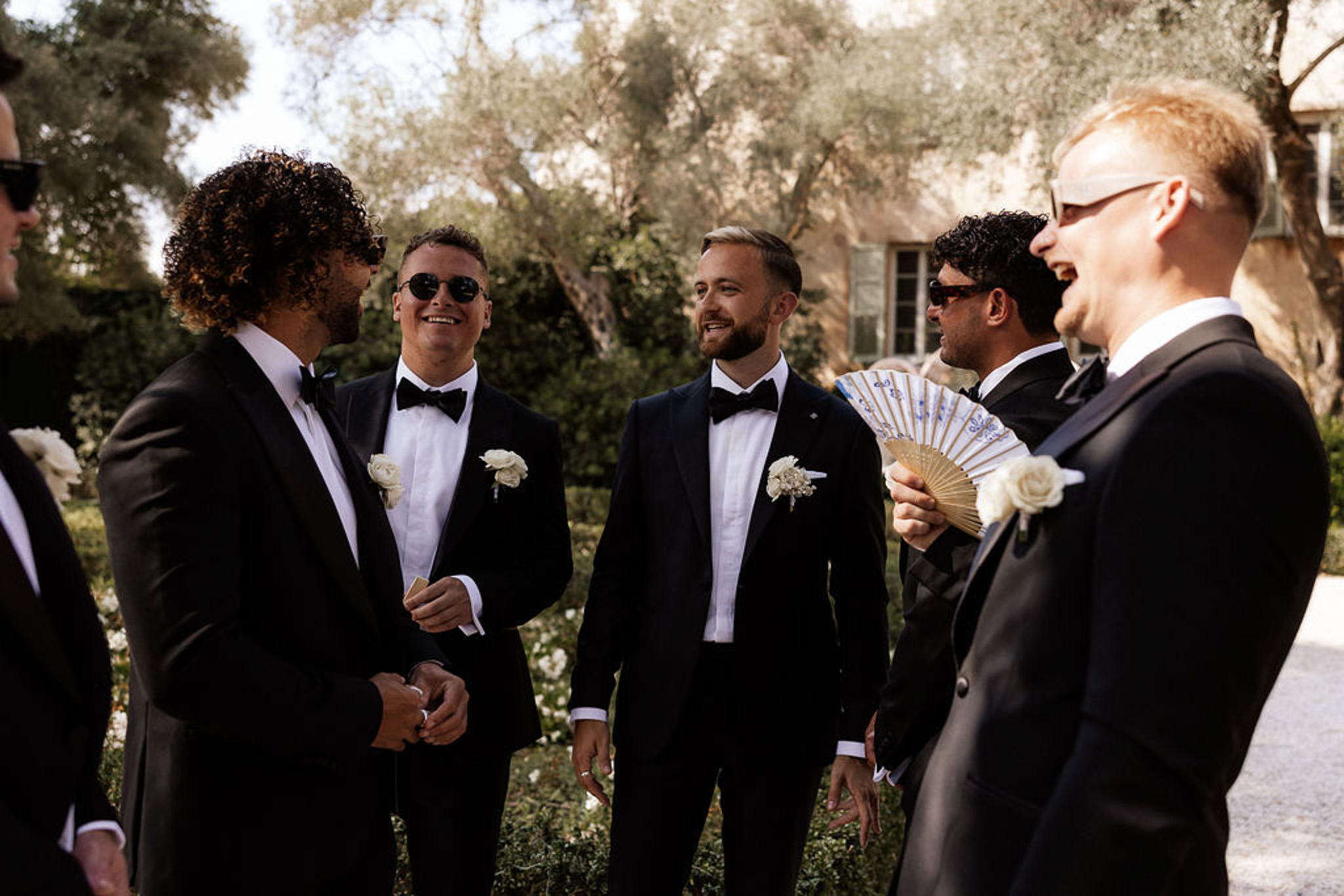 Groom and groomsmen in black tuxedos with white boutonnieres at Mediterranean garden wedding