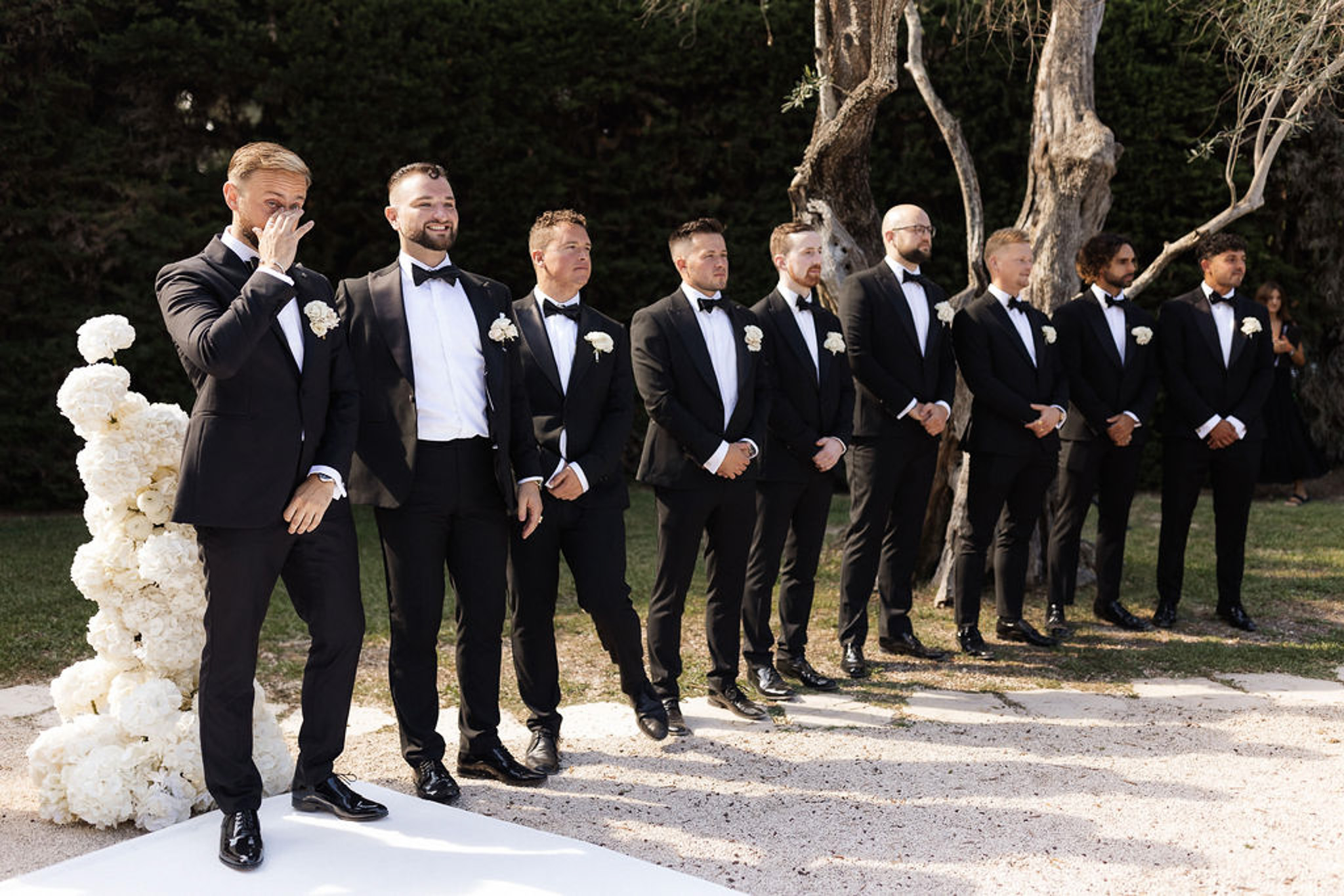 Groom and groomsmen waiting at altar during outdoor garden wedding ceremony with white floral arrangements