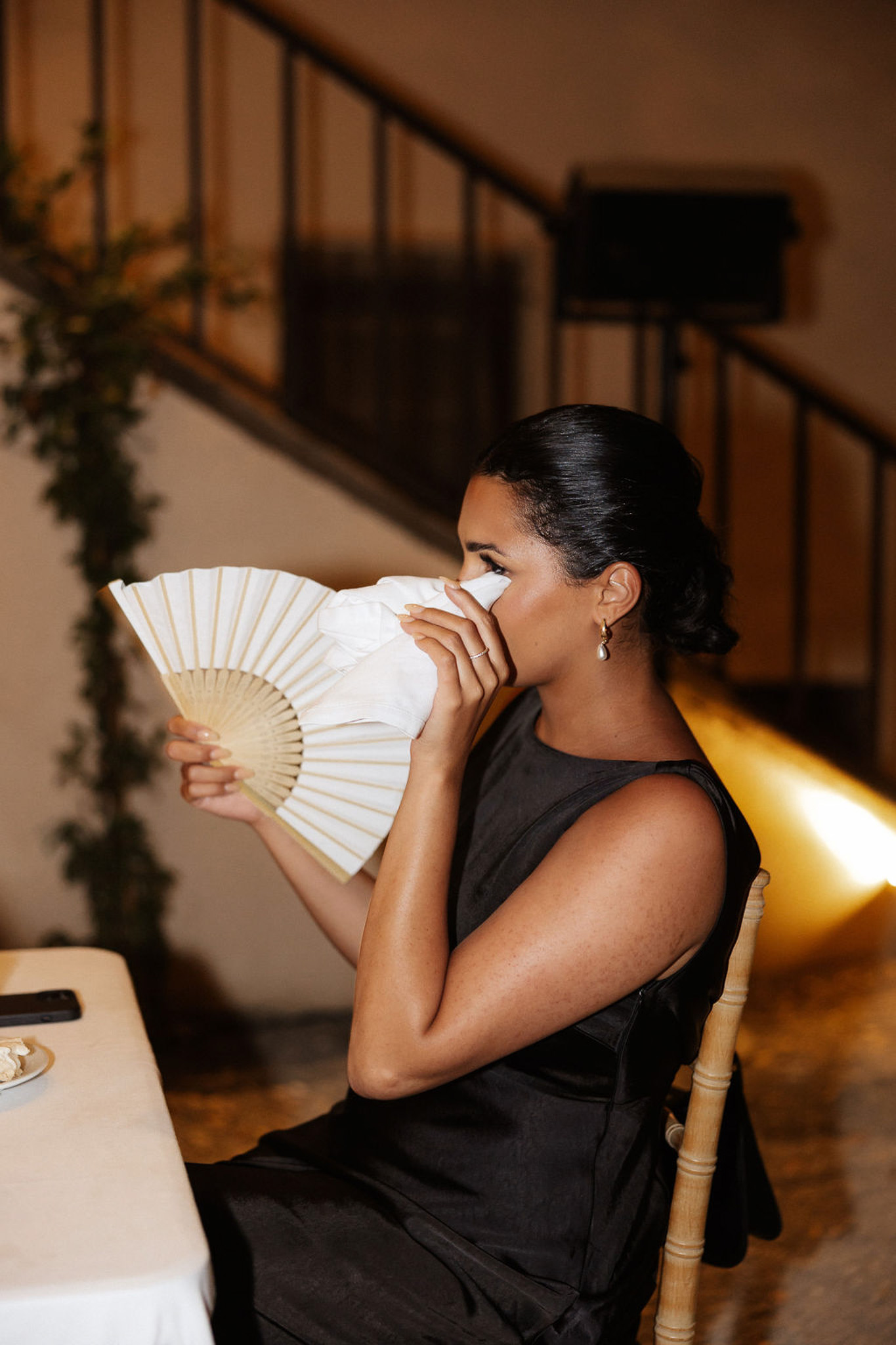 Wedding guest with fan during indoor reception at elegant venue