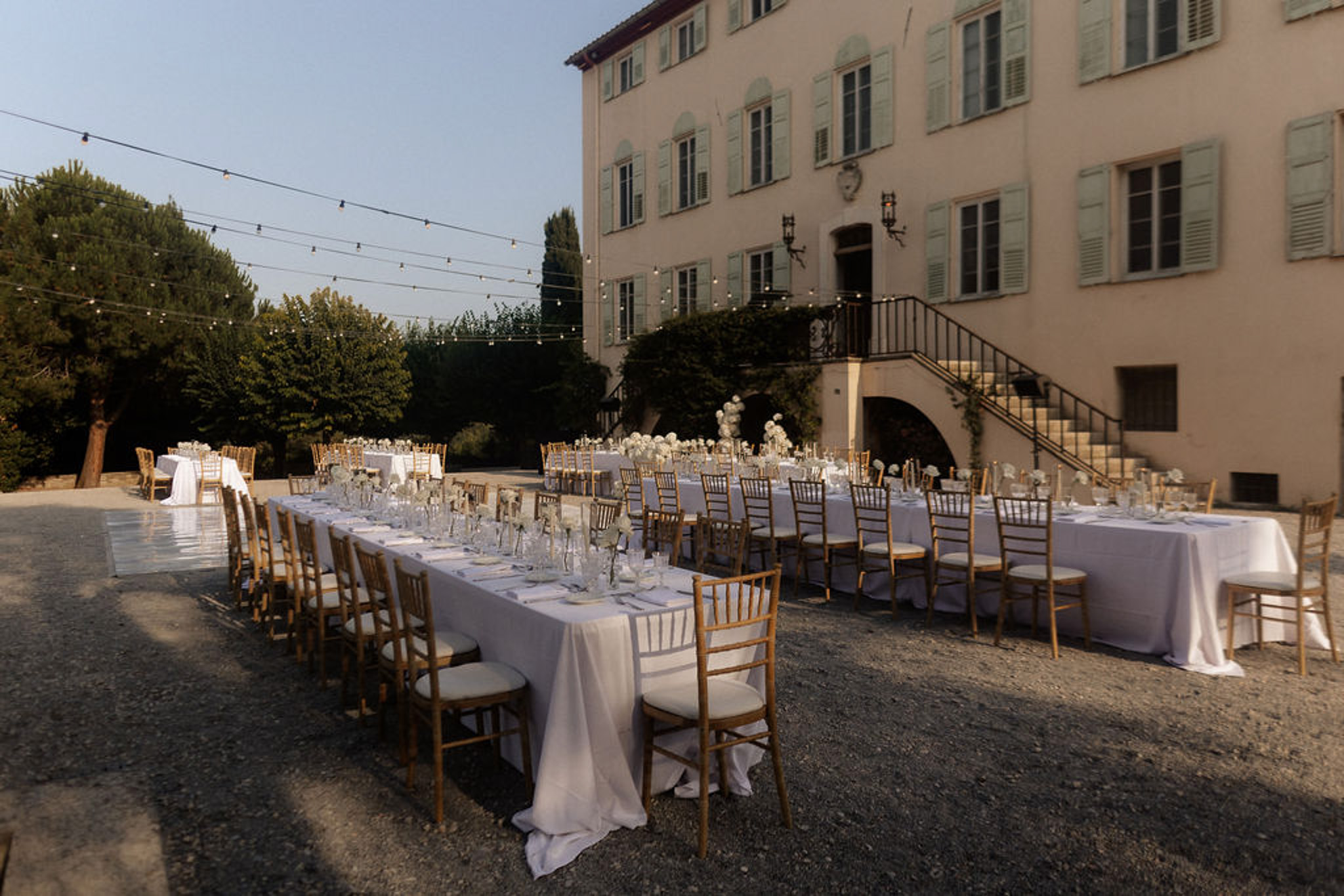 Outdoor reception setup in historic Italian villa courtyard with long banquet tables and string lights