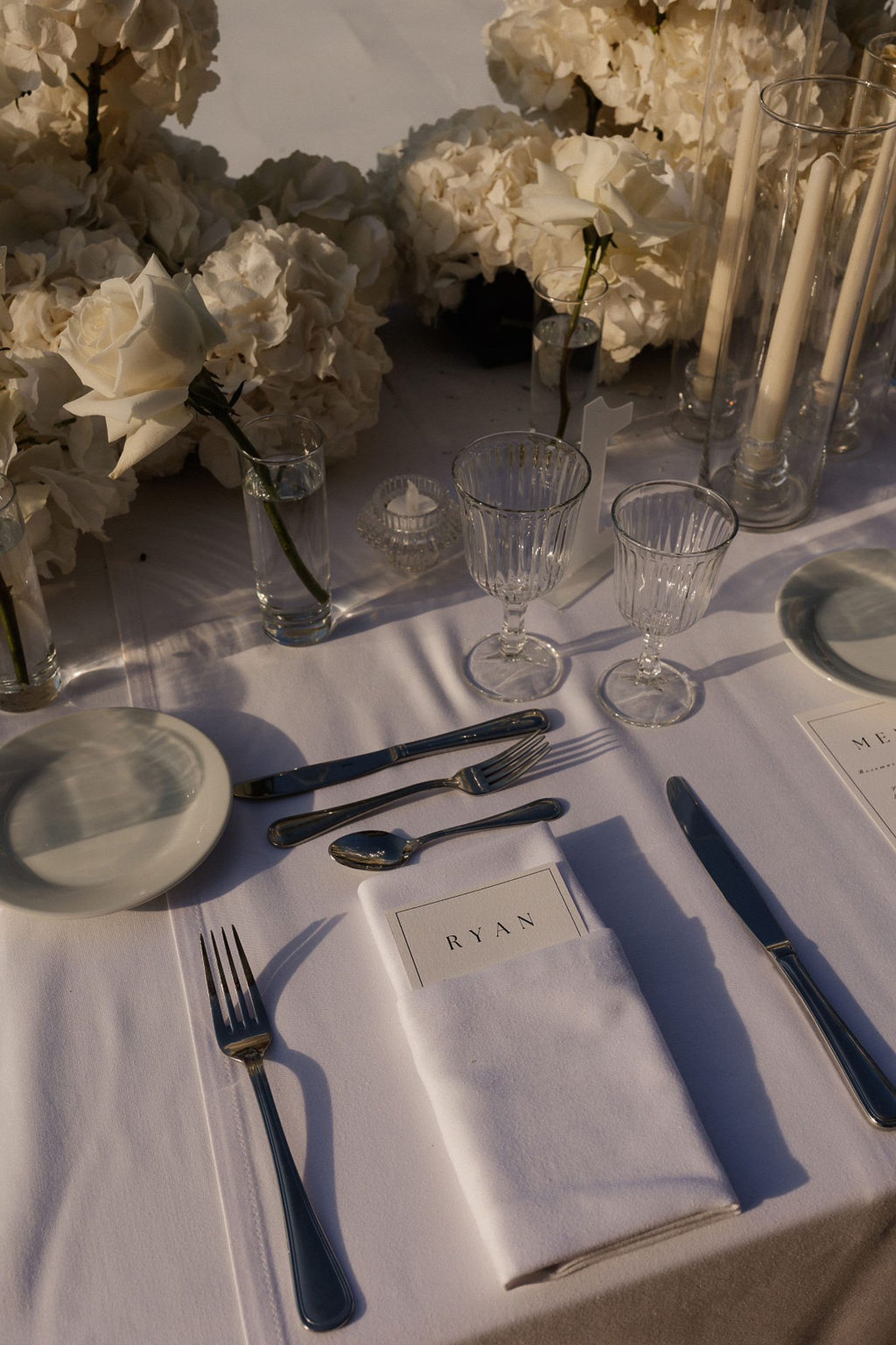 Reception table setting with white linens, gold flatware, and cream roses at wedding venue