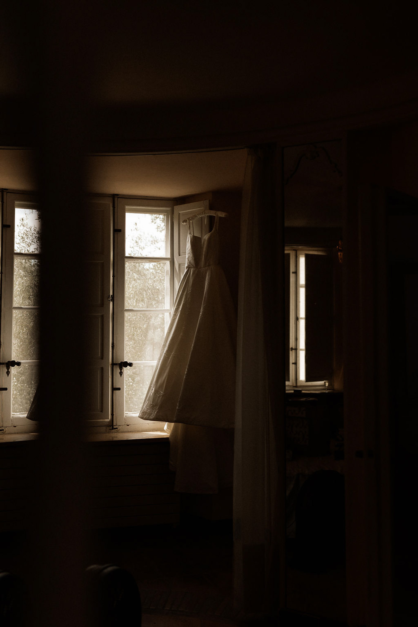 Ivory wedding dress hanging on wooden rail near French doors in bridal suite
