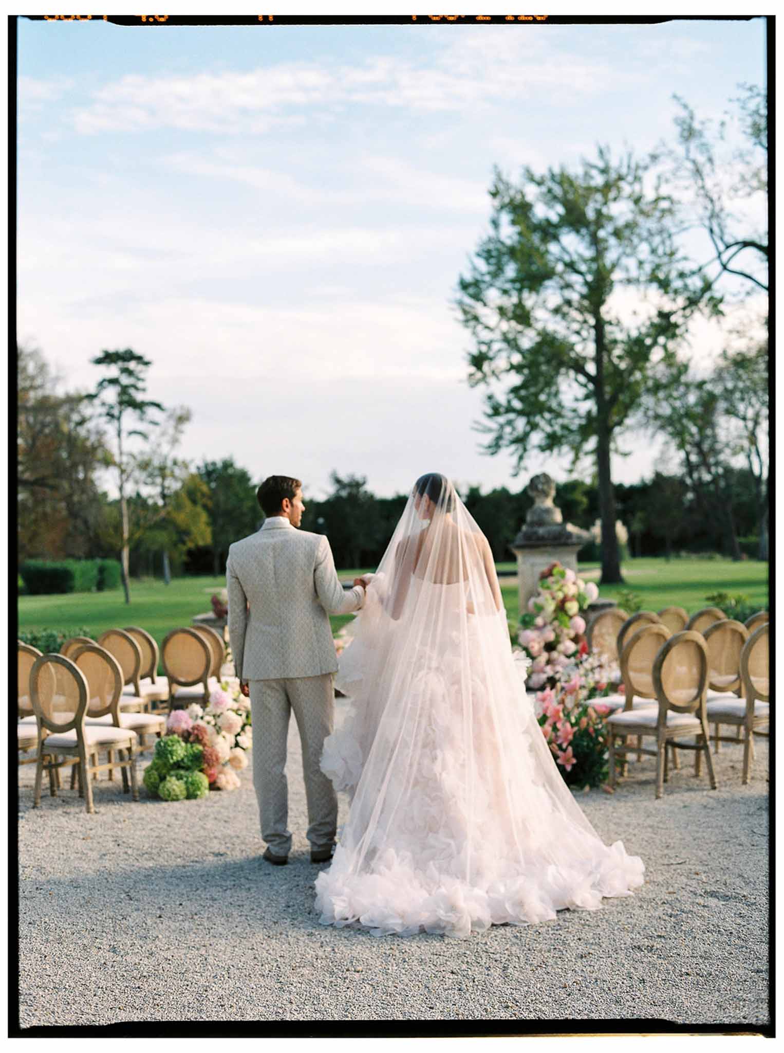 Couple at altar during outdoor wedding ceremony in manicured park with Bentwood chairs and floral arrangements