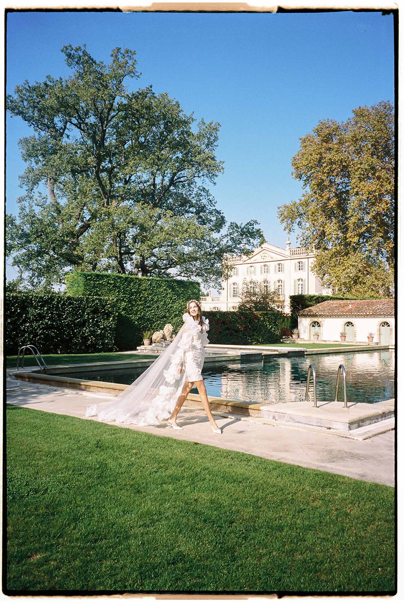 Bride in ivory wedding dress posing beside swimming pool at classical European estate with autumn foliage