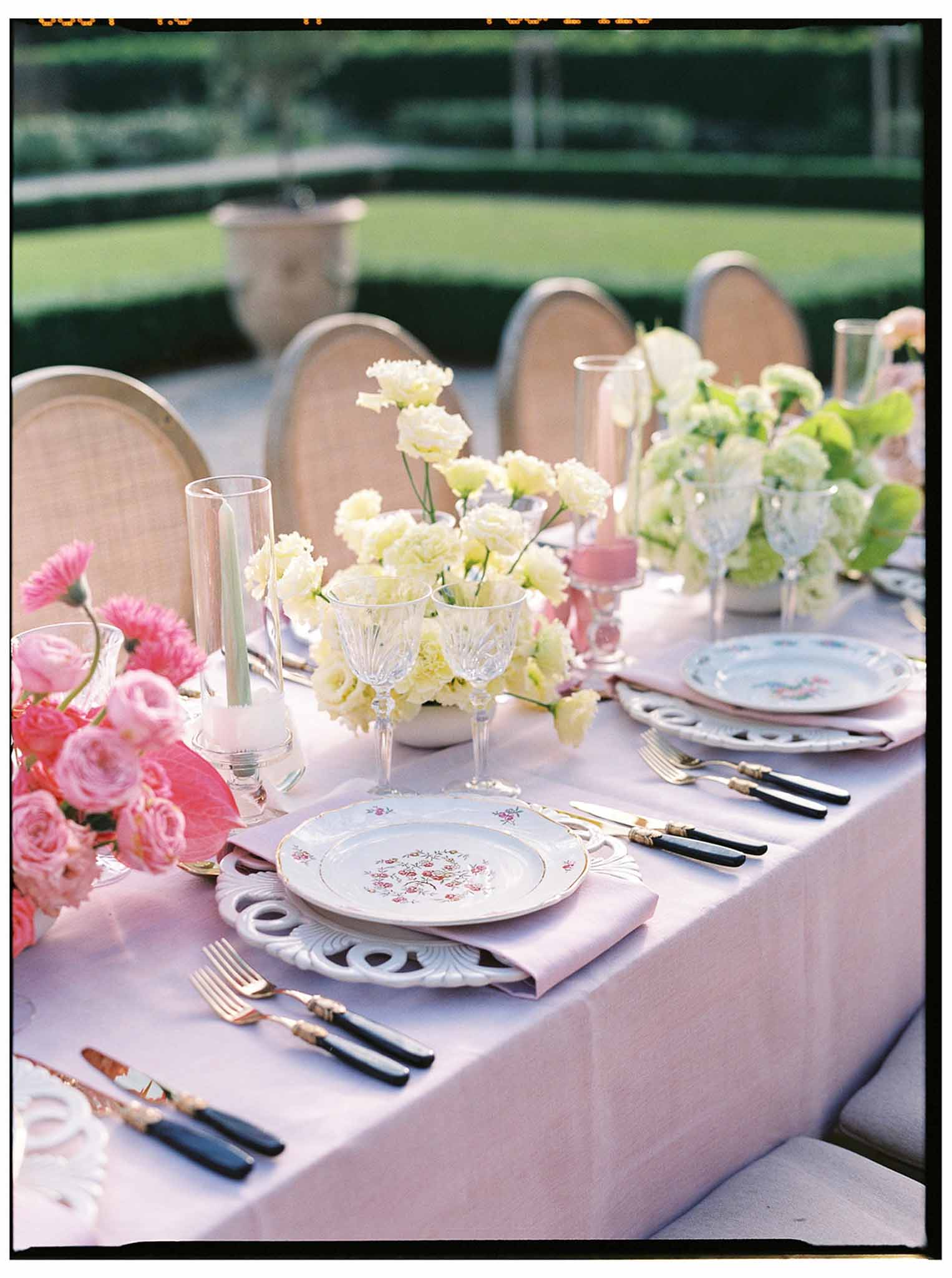 Reception table setting with pink linens and floral centerpieces in formal garden