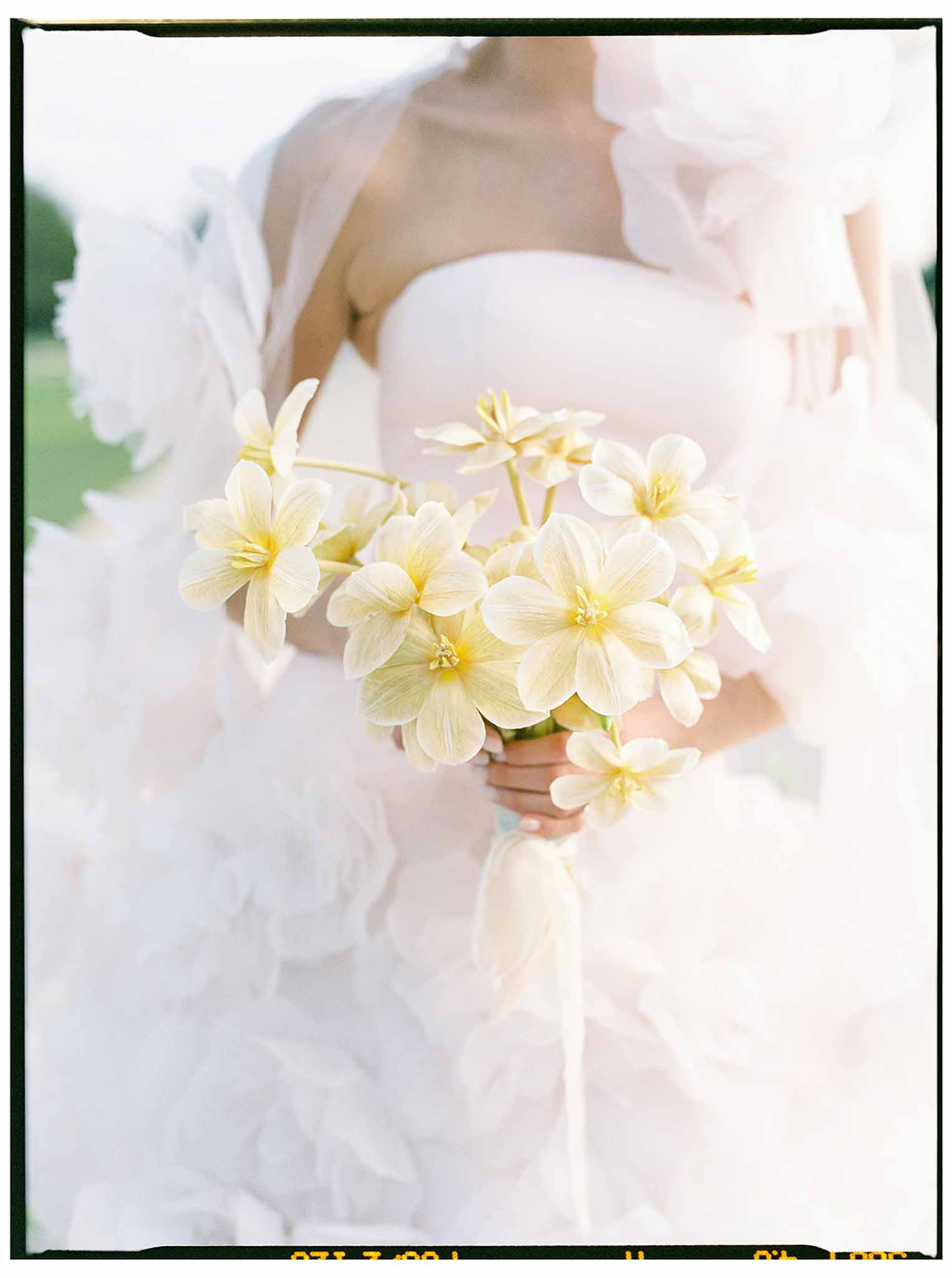 Bride holding cream and pale yellow dahlia bouquet in garden setting