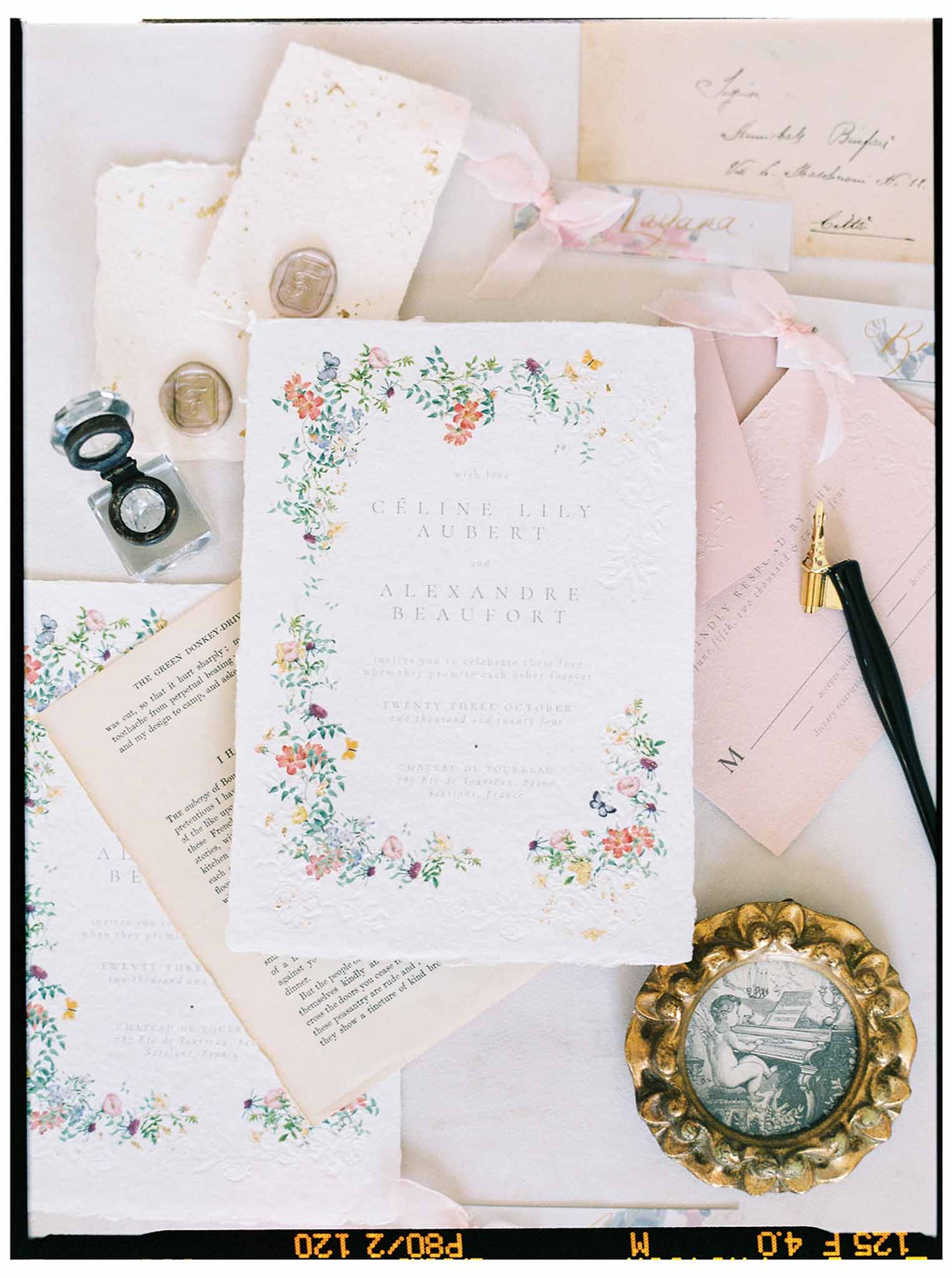 Wedding invitation suite flat lay with botanical floral borders and gold accents for Céline and Alexandre