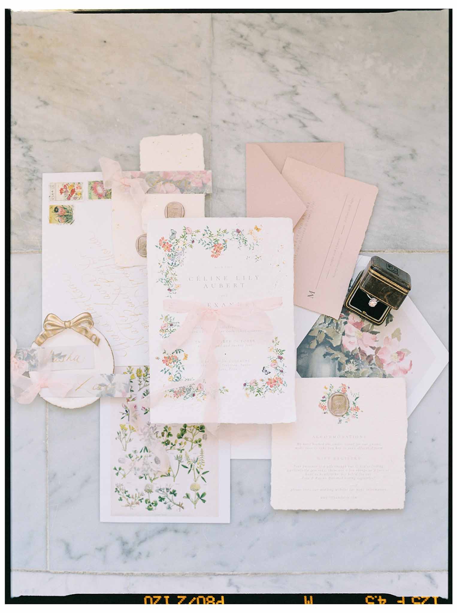 Wedding stationery flat lay with blush envelopes and floral watercolor invitations on marble surface